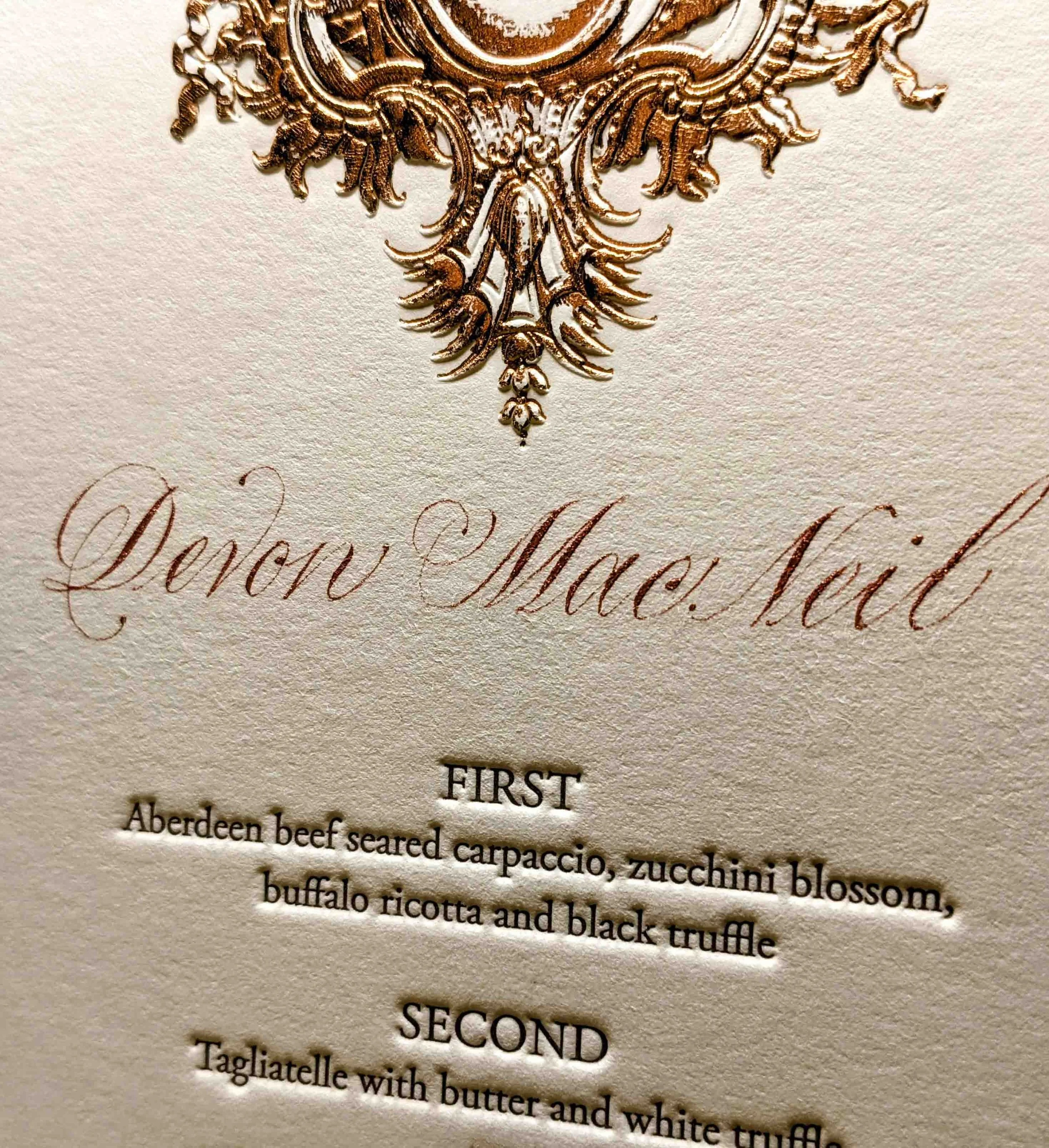 A foil embossed dinner menu hand lettered in a custom-matched, bronze and copperplate script calligraphy.