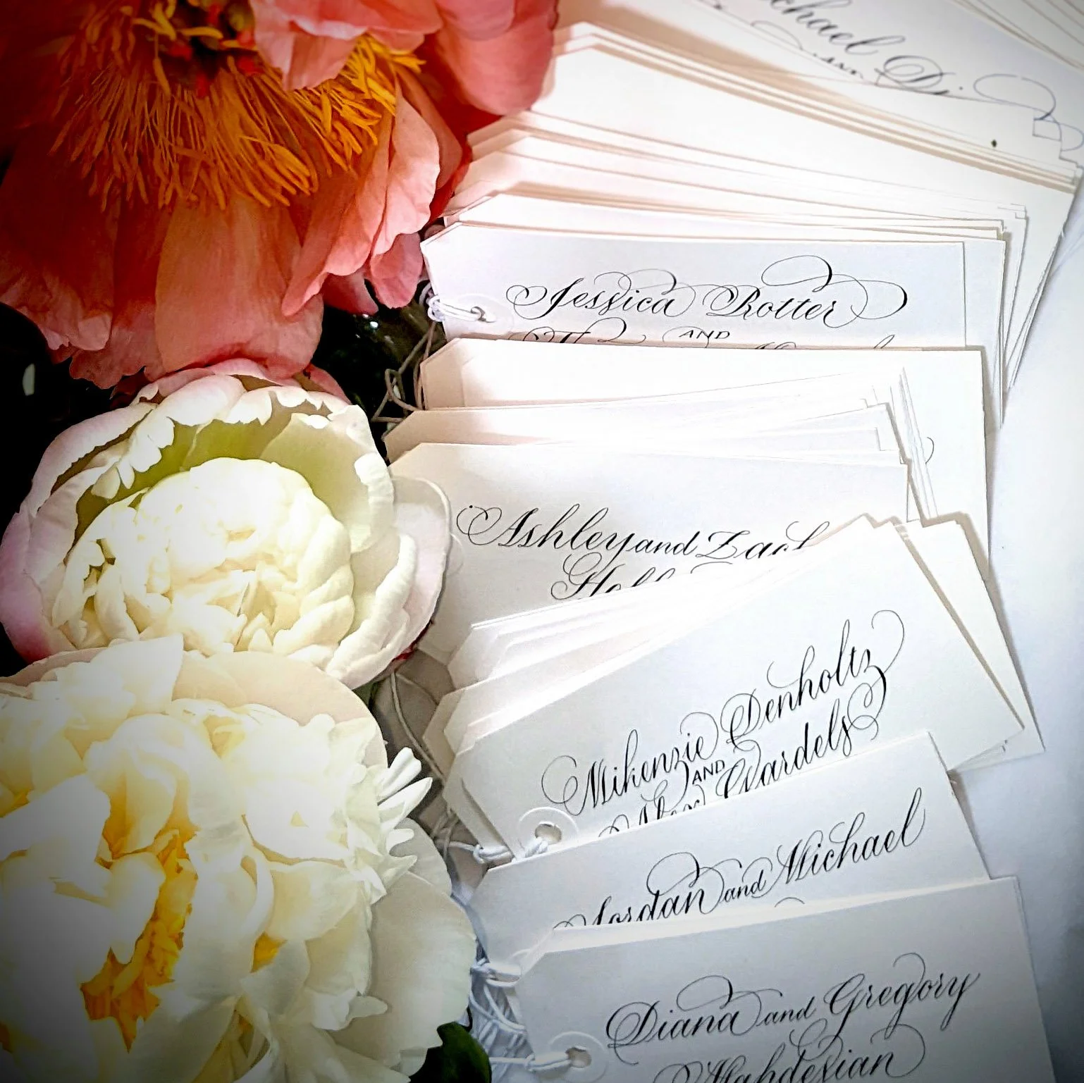 An assembly of white peonies and white gifts tags to personalize wedding take-home gifts.