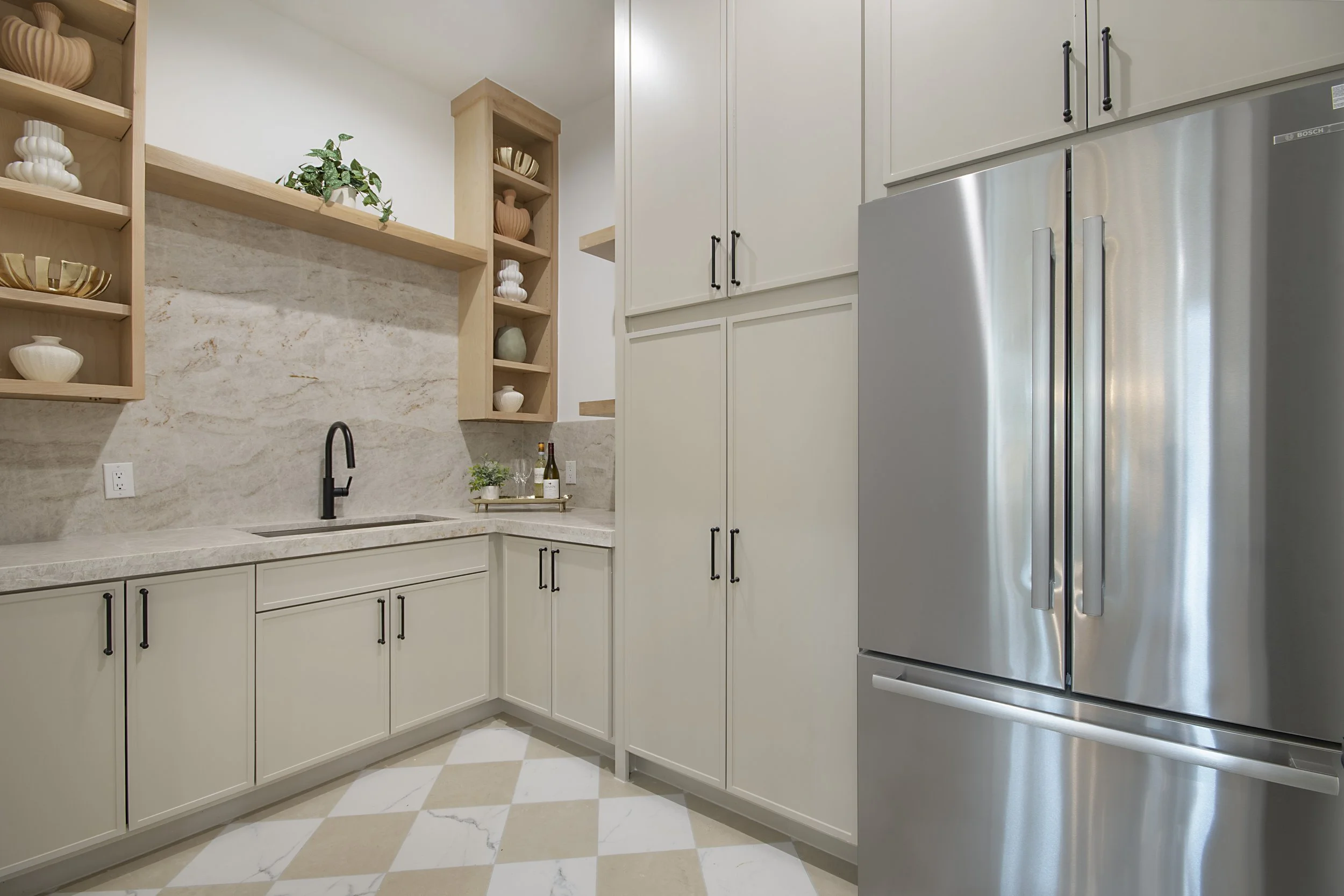 Modern kitchen with white cabinets, black handles, a beige marble backsplash, open wooden shelves with decorative vases and plants, a black faucet, and a stainless steel refrigerator.