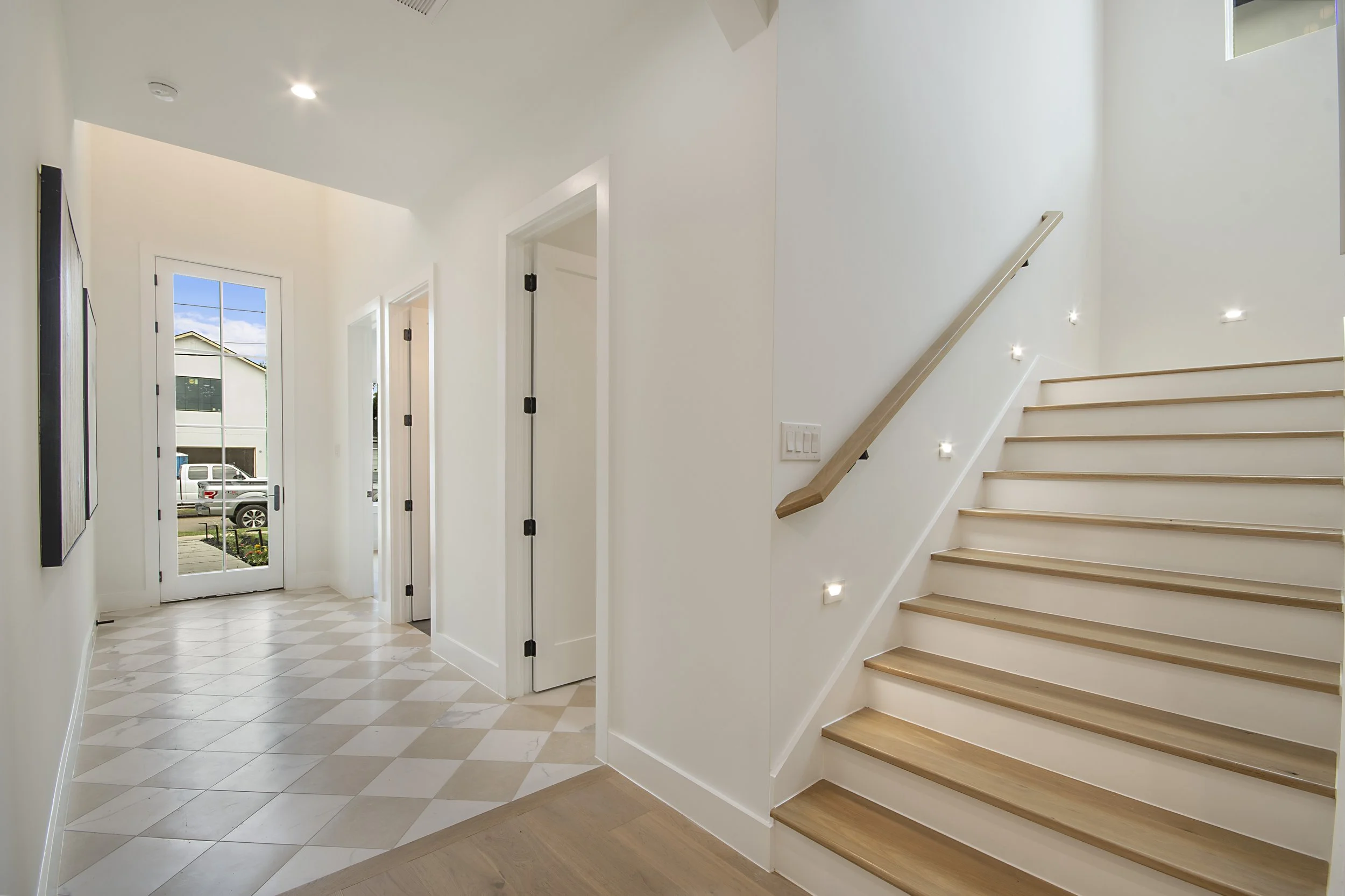 Modern entryway with white walls, wooden stairs, a glass door, and diamond-patterned tile floor.