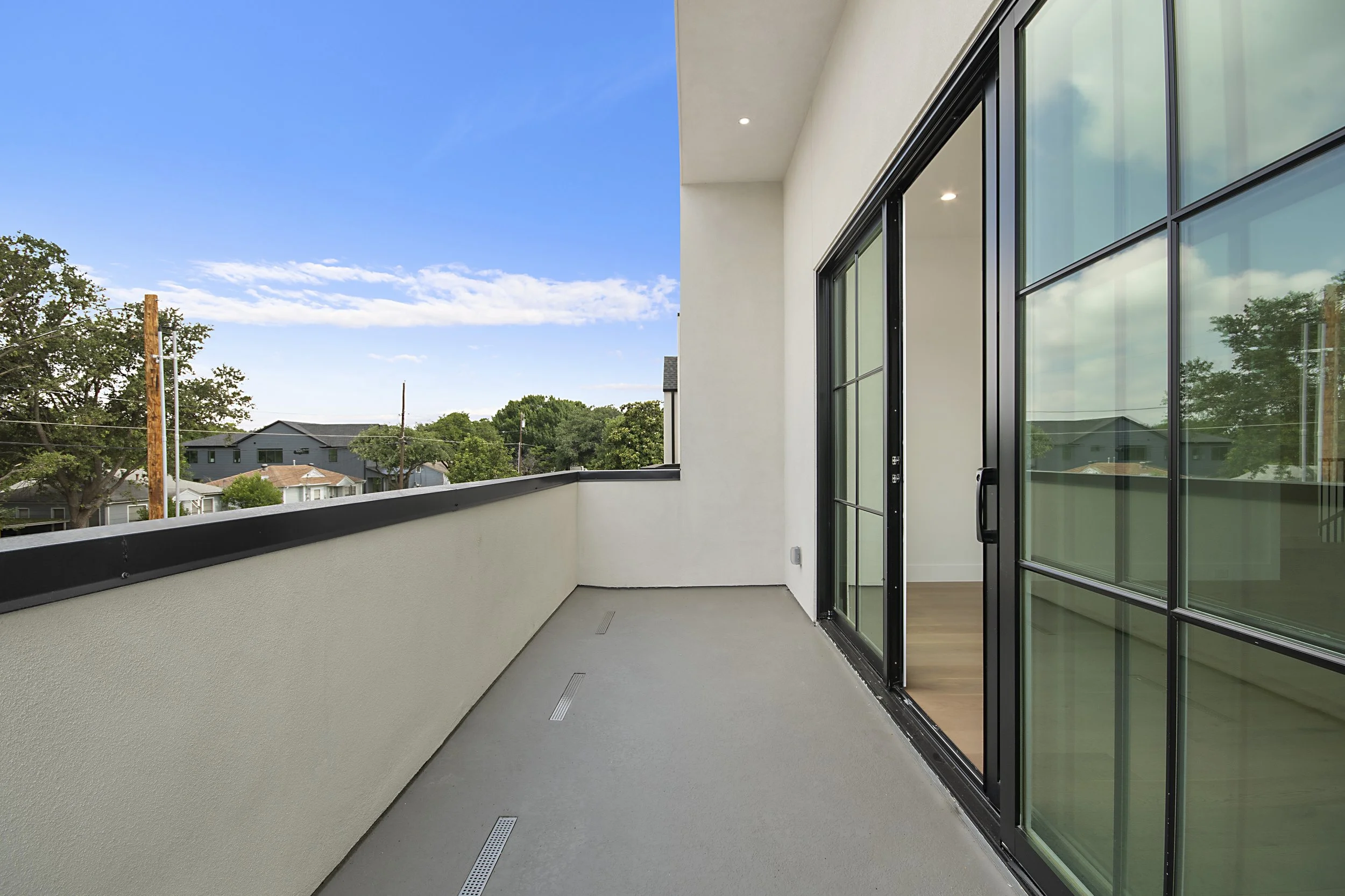 Balcony with sliding glass doors and a view of trees and houses under a blue sky.