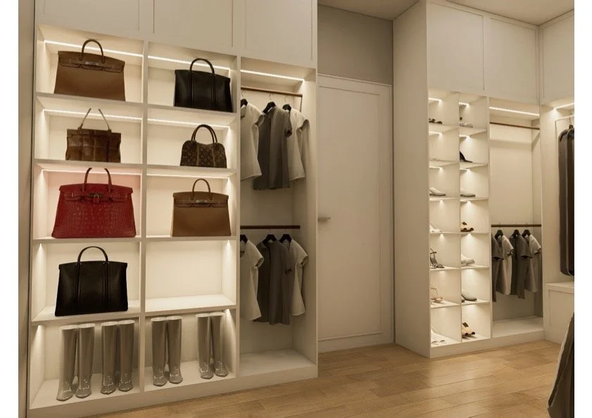Elegant walk-in closet with white shelves displaying handbags, shoes, and clothing, and wooden flooring.