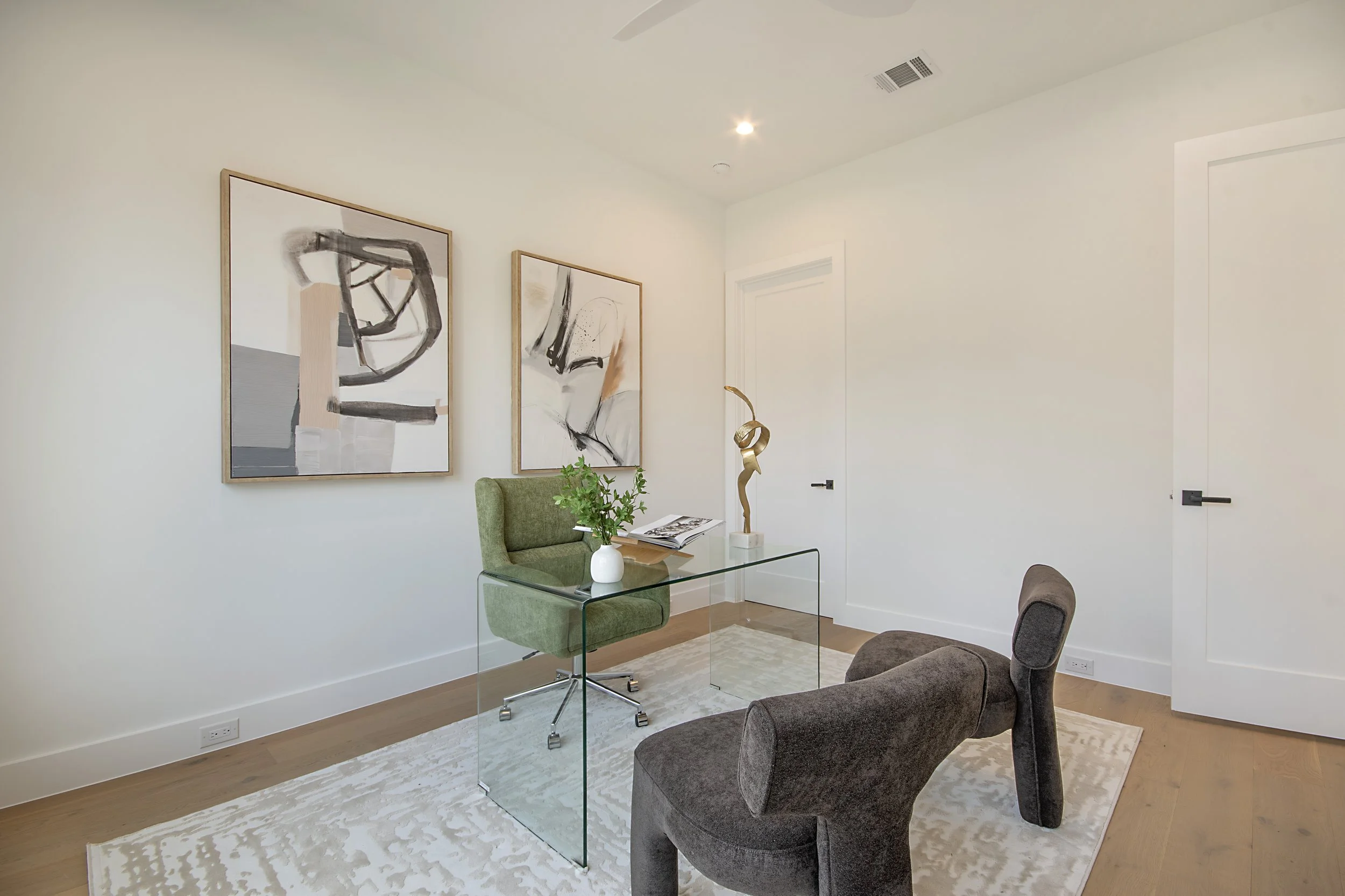 A modern office space with a glass desk, green office chair, and artwork on the white walls.