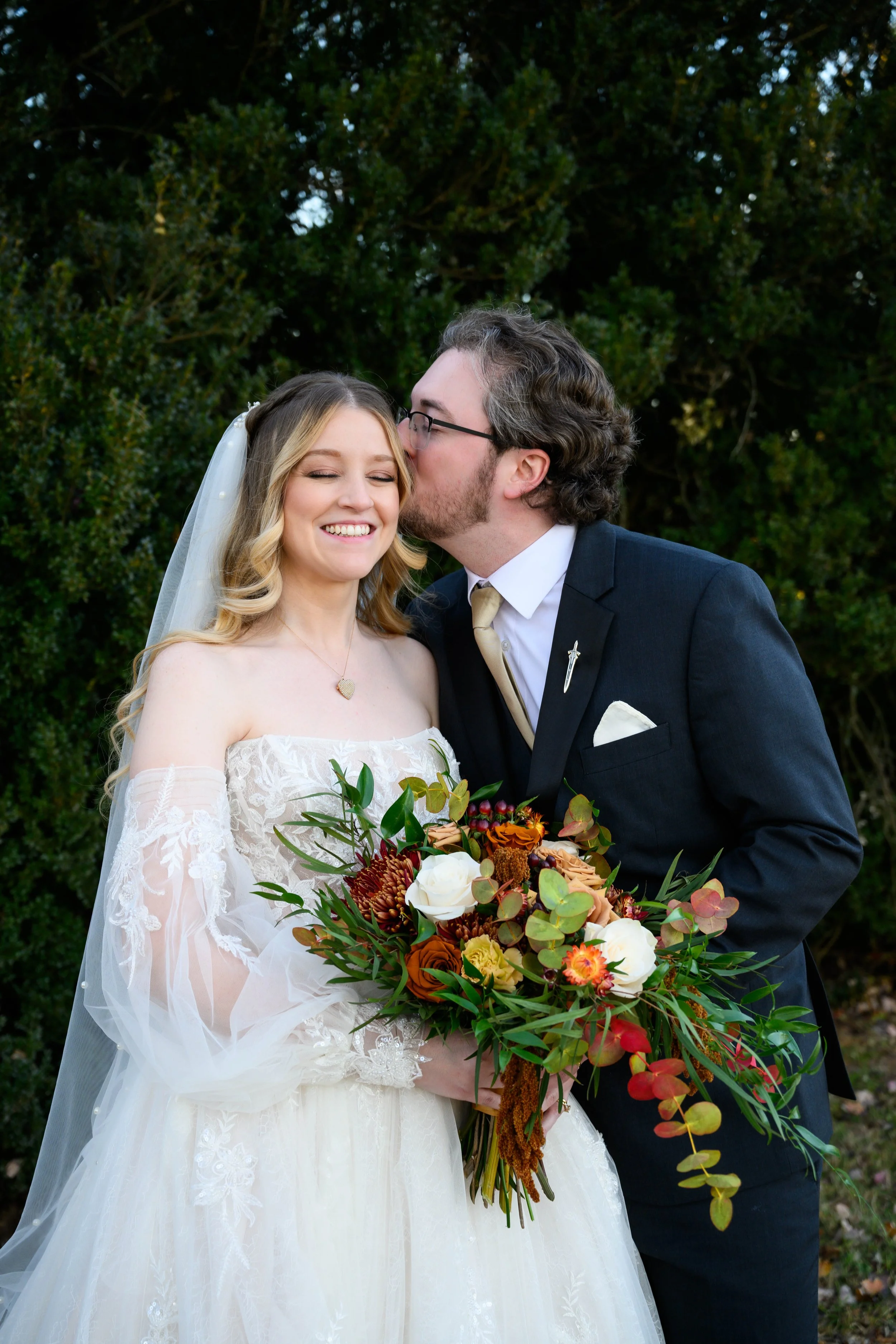Bride smiling with Groom. Her hair is in a cascading braid and wearing a veil.