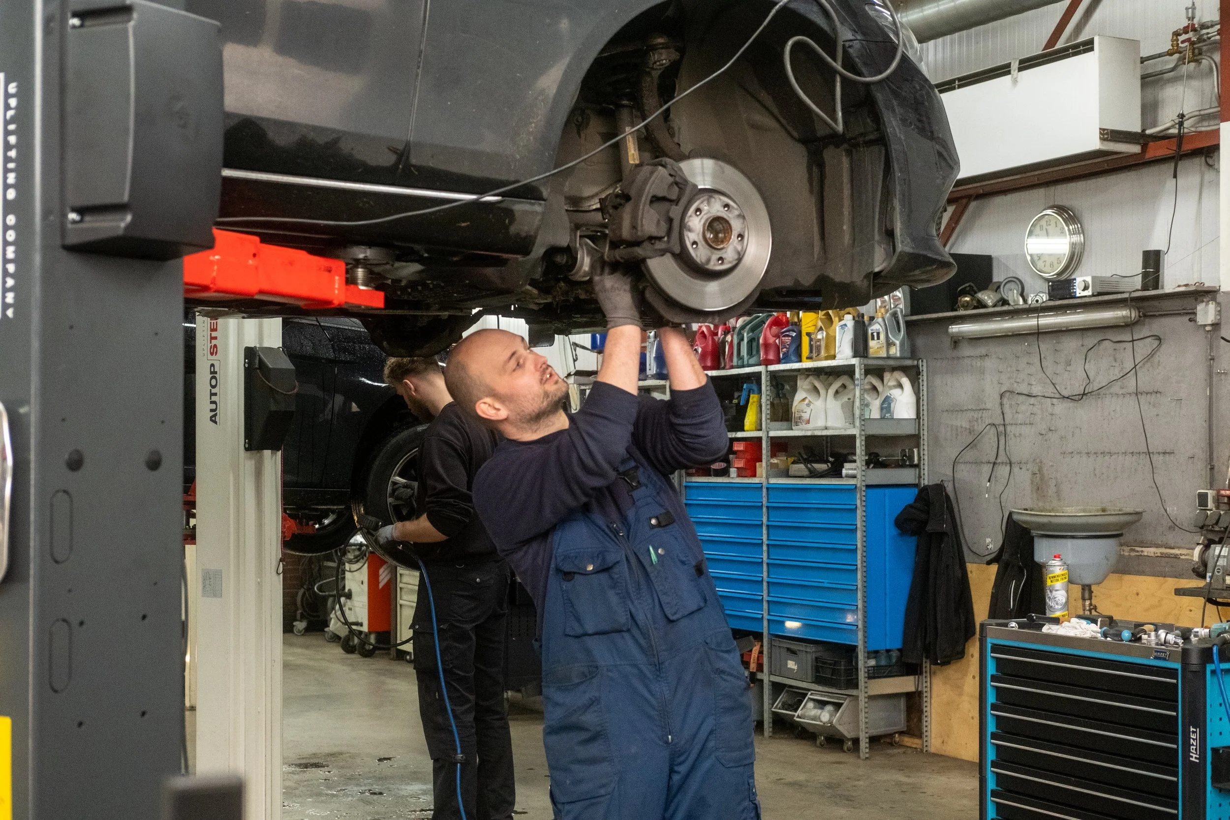 Monteur werkt aan remmen onder een auto in de werkplaats van Garage van Beek Soesterberg, vacature leerling autotechnicus