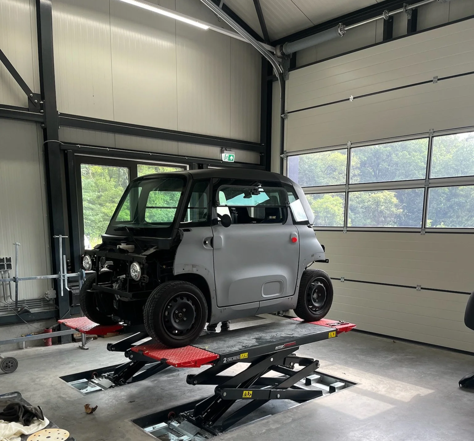 Een kleine elektrische auto wordt in een garage op een automatische lift gehesen voor onderhoud.