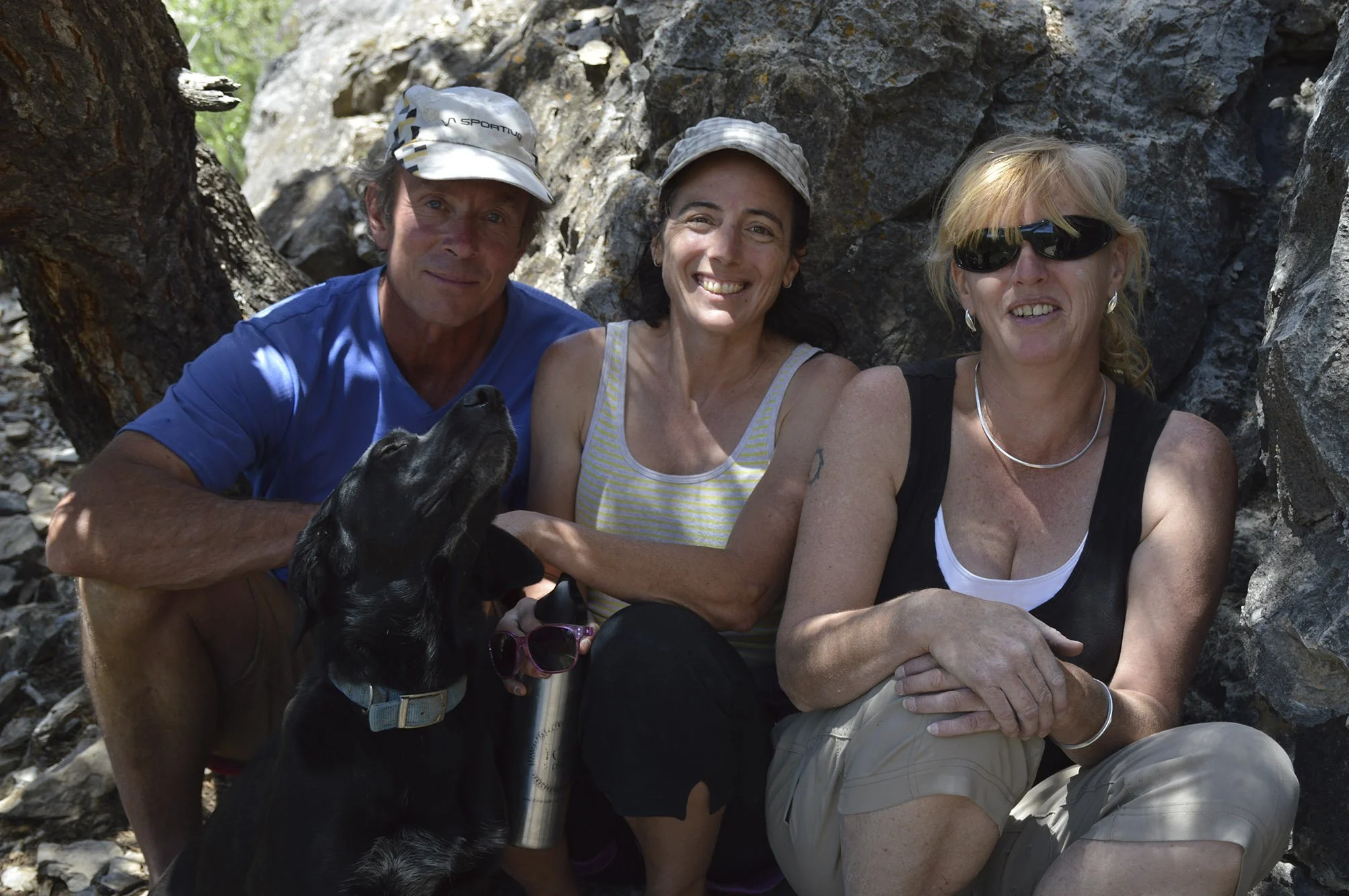 Wolverine Publishing owners Jeff, Amber, and Fiona sit at the base of a cliff in the shade of a tree with their dog