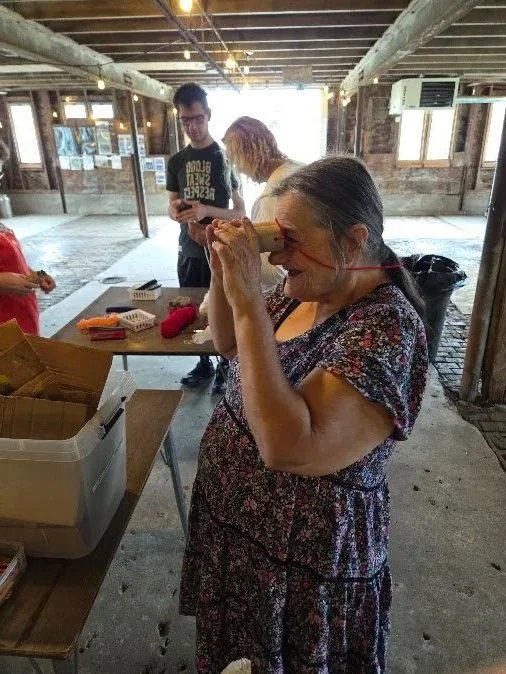 Adult woman smiles as she looks through toilet paper tube binoculars she made.