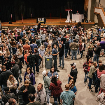 Crowd of people gathered in a large indoor event space with a stage in the background and a VIP sign.