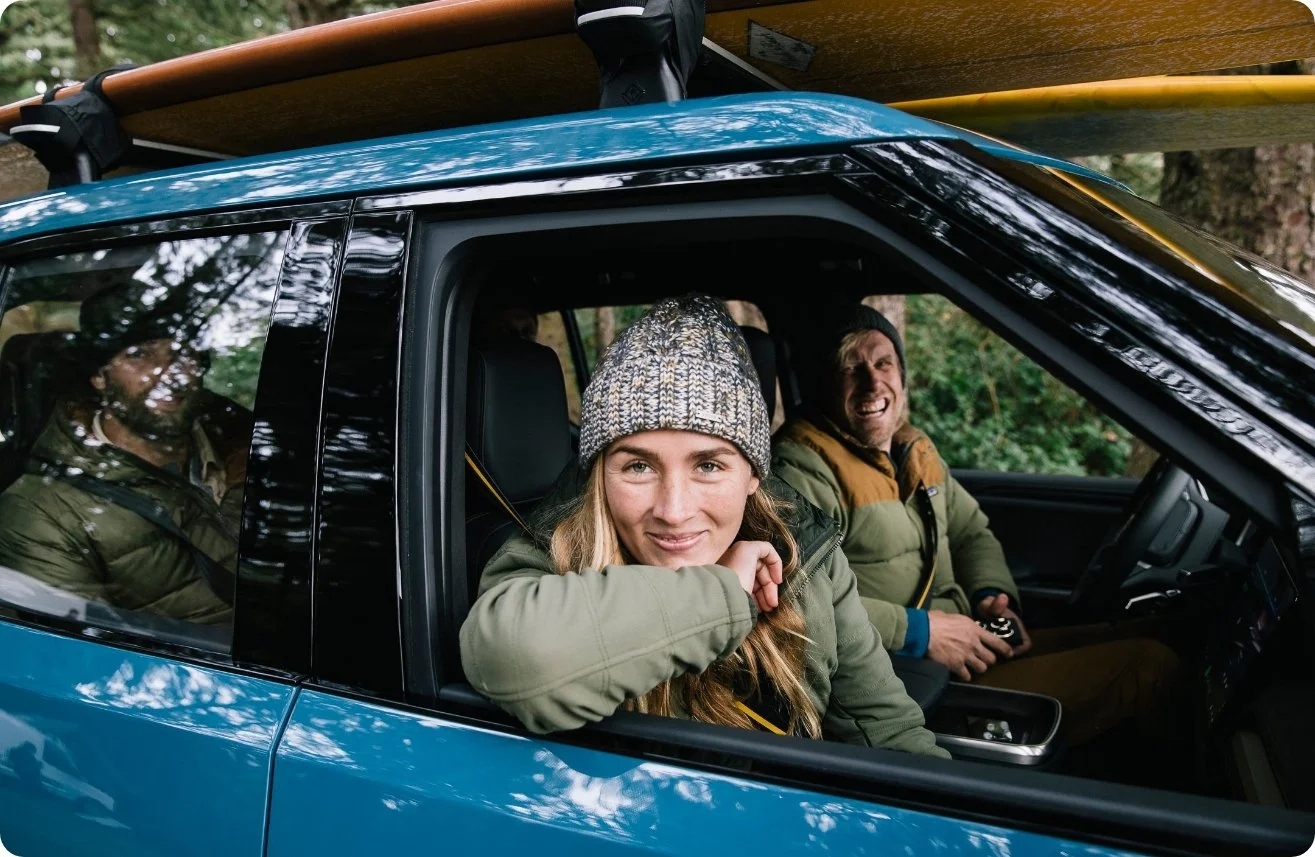 Two people smiling from the window of a blue Rivian