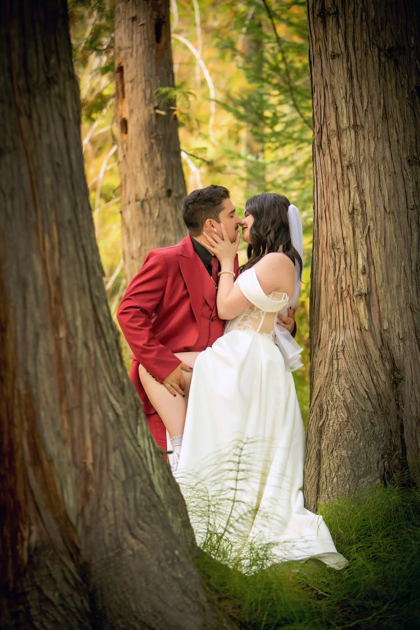 Bride and groom sharing a passionate, intimate moment between towering cedar trees at Cedar River Wedding Venue in Priest River, Idaho, surrounded by dappled sunlight and the serene forest atmosphere.