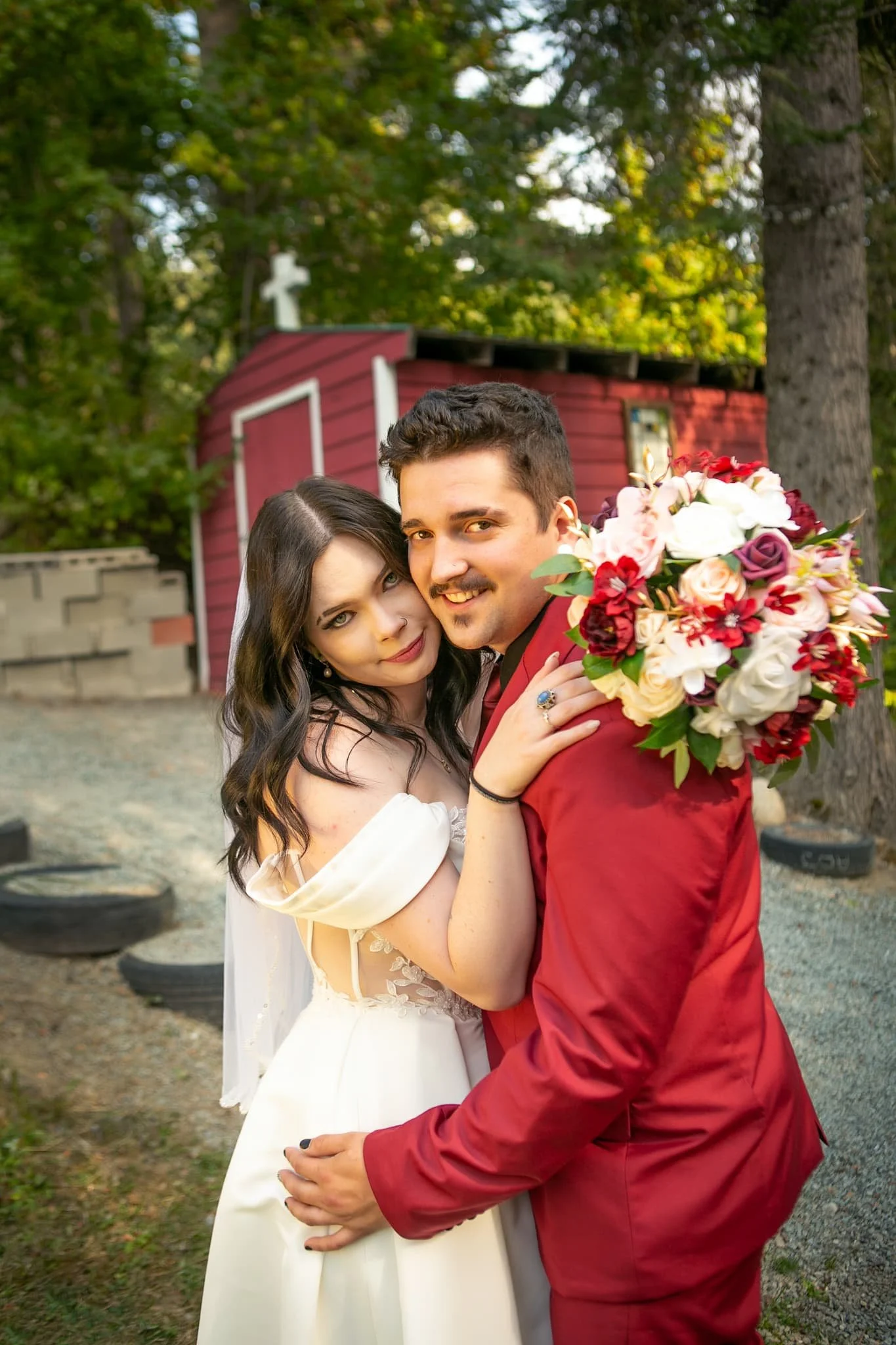 Bride and groom posing in front of the charming little red church at Cedar River Wedding Venue in Priest River, Idaho, surrounded by forest and serene outdoor scenery for a timeless, intimate portrait.
