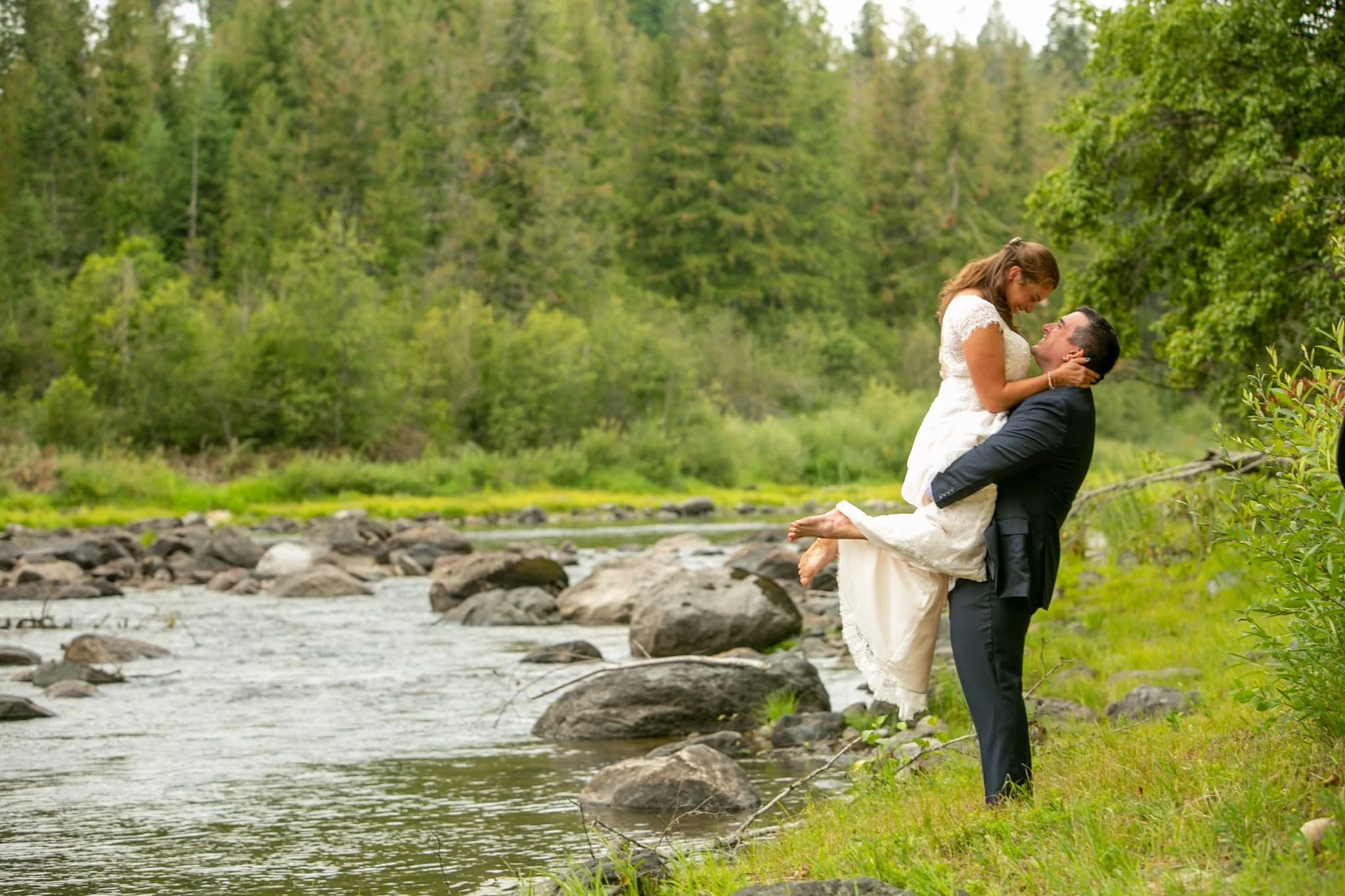 Spokane area couple embracing along the riverbank at Cedar River Weddings a dreamy outdoor wedding venue with bohemian charm