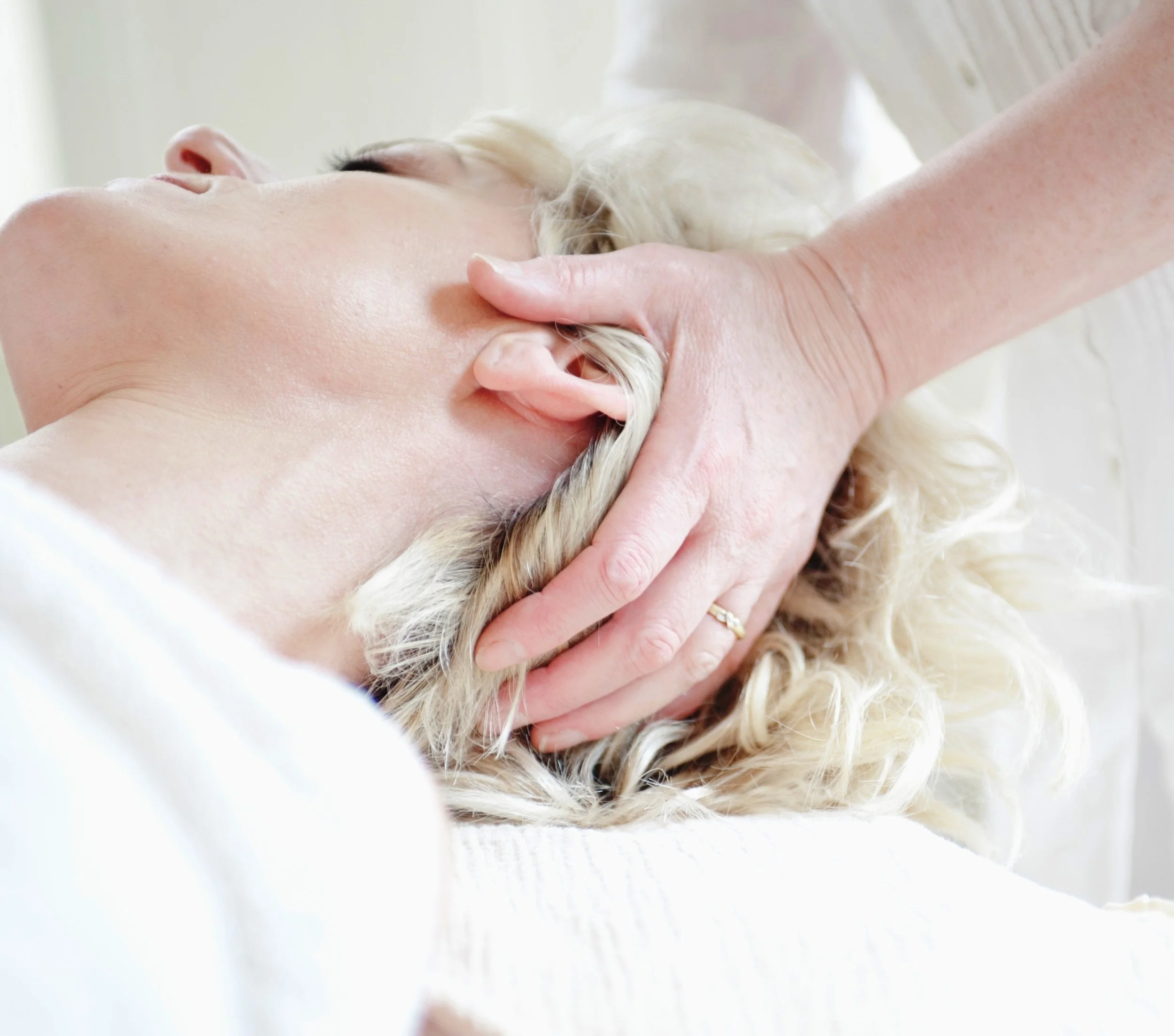 A woman receiving a massage on her neck and shoulder area, lying on her back with a relaxed expression.