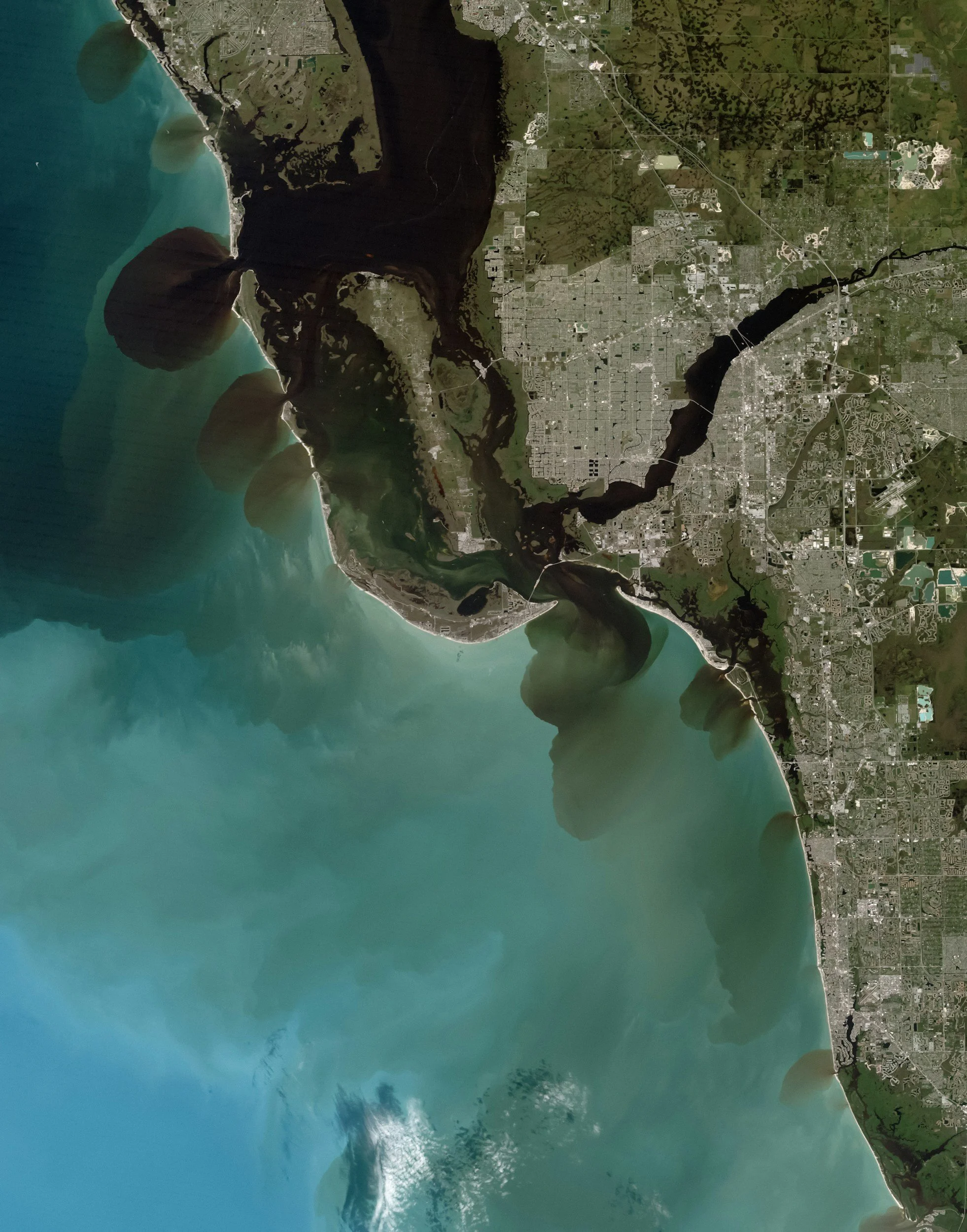 Satellite image of a coastal area with a river flowing into the ocean, showing land, water, and urban development.