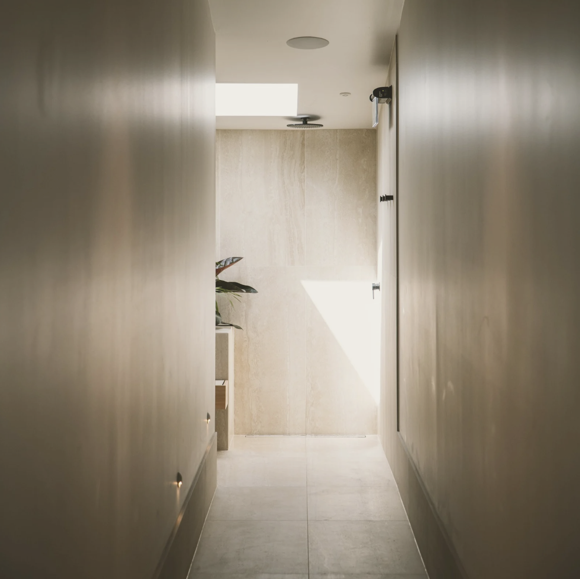 A narrow hallway leading to a sunlit room with beige walls and floor.