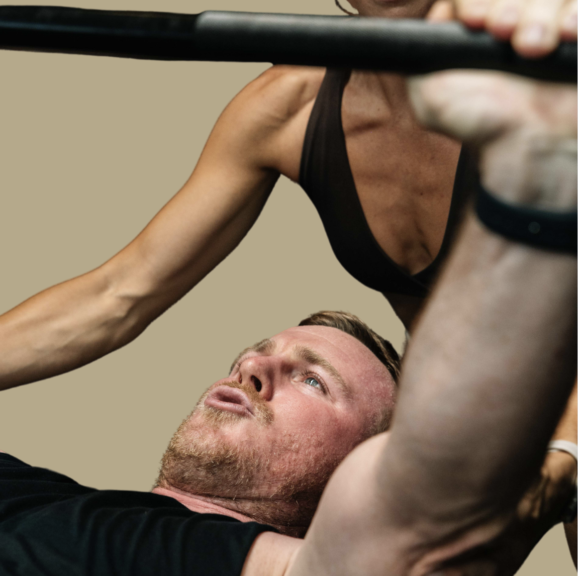 A man lying on a workout bench performing a bench press exercise with a woman assisting or spotting him.