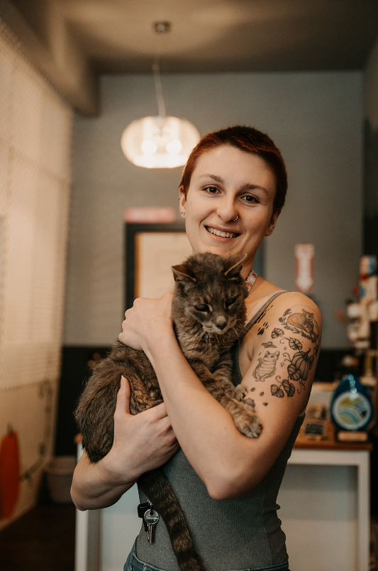 Emily, the owner of Paws and Pumpkins Rescue, is holding the resident cat, Saturn in her arms and smiling at the camera.