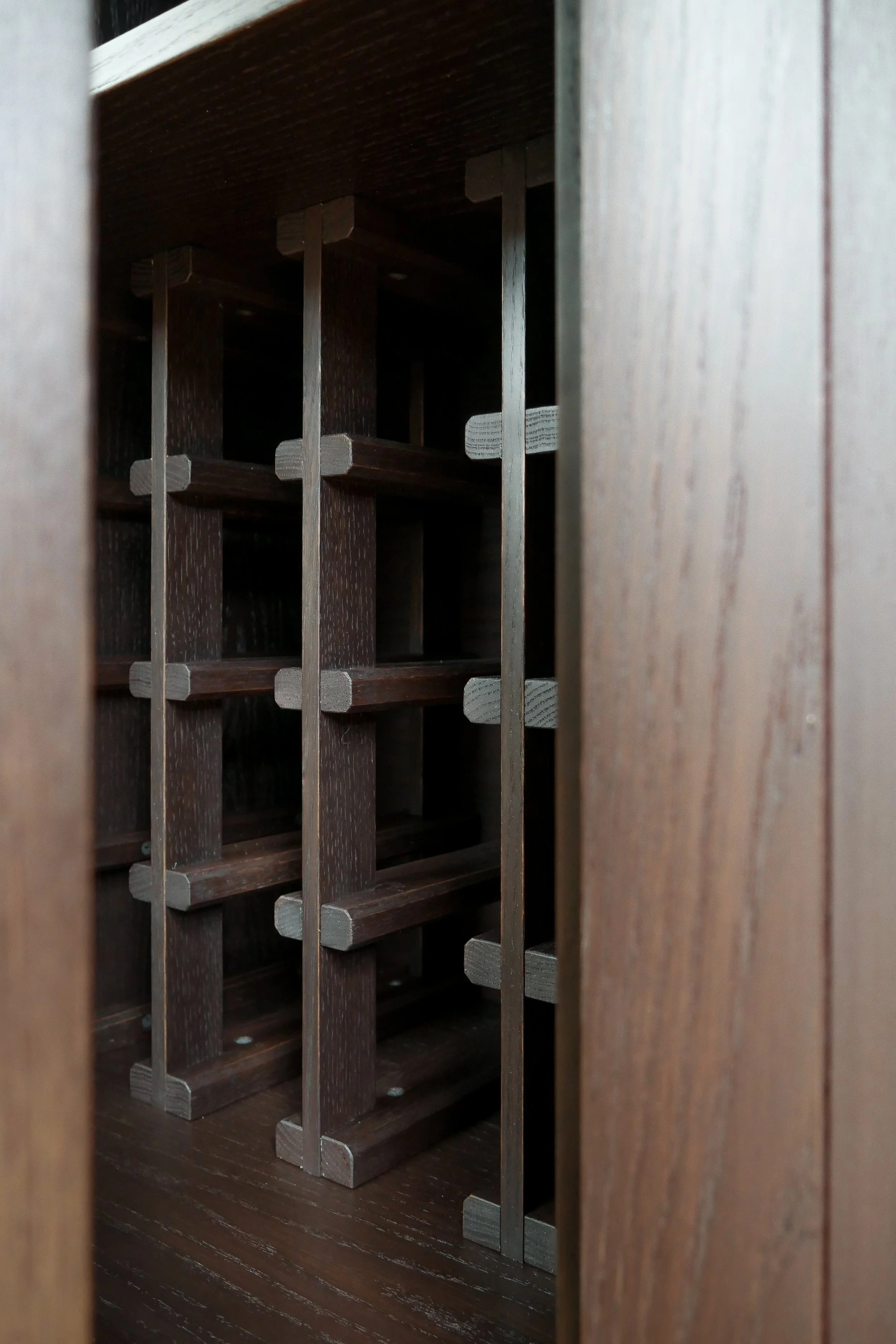 A wooden wine rack seen through a narrow opening, with shelves for bottles visible inside.
