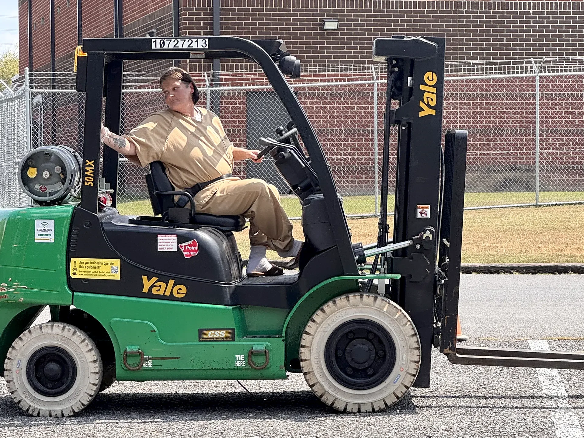A woman operates a forklift in a parking lot.