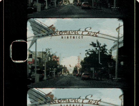 View of a city street through a car's rear window with a 'Rosemont Square District' sign overhead.