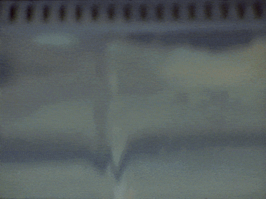 Tornado forming over a body of water, seen from below, with a cloudy sky above.