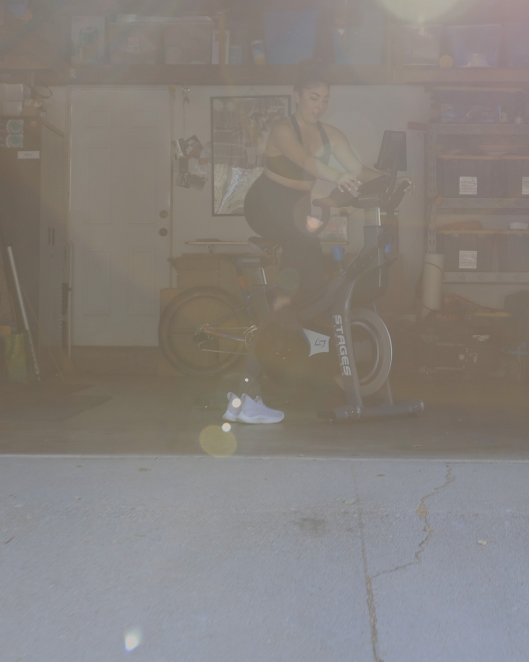 Woman in workout attire riding a stationary exercise bike in a garage or storage room.