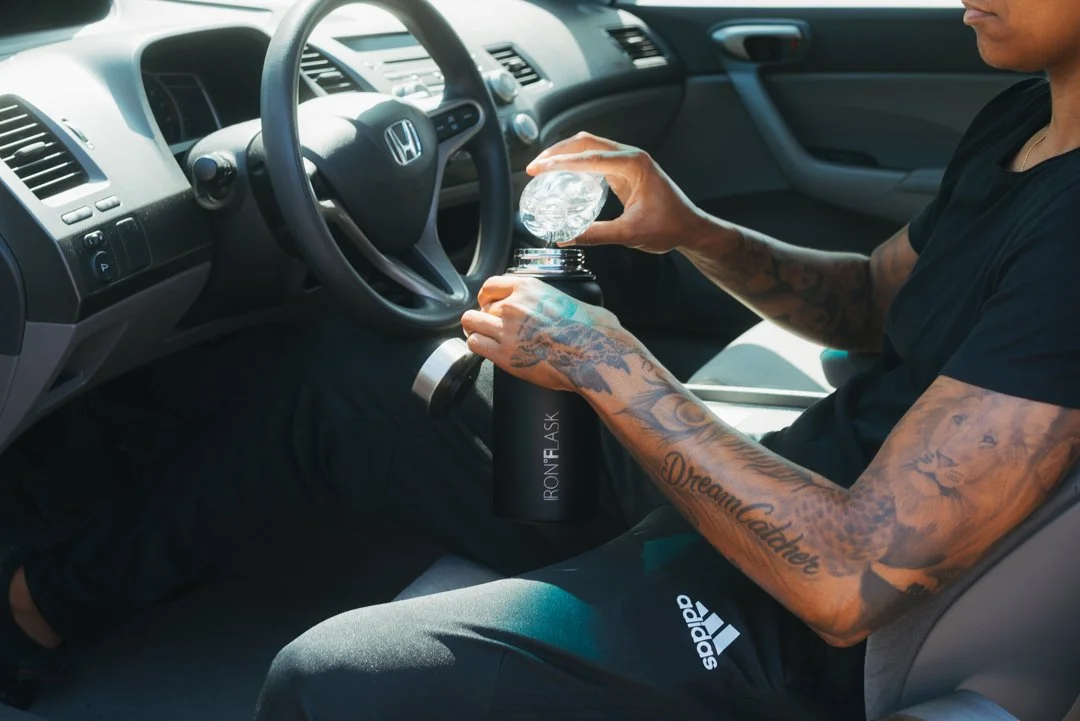 Person with tattoos filling a water bottle from a water cooler in a car.