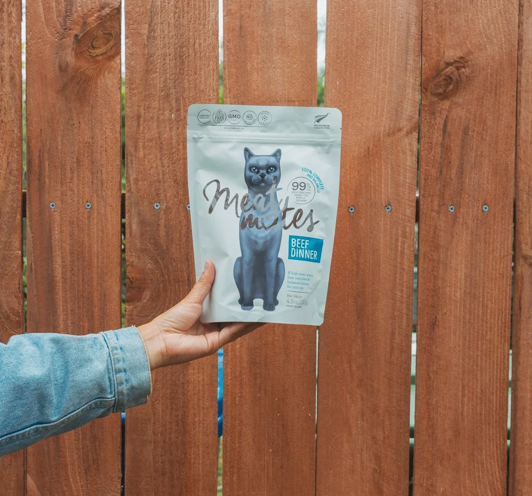 Person holding a bag of Meat Mutes beef dinner pet food in front of a wooden fence.