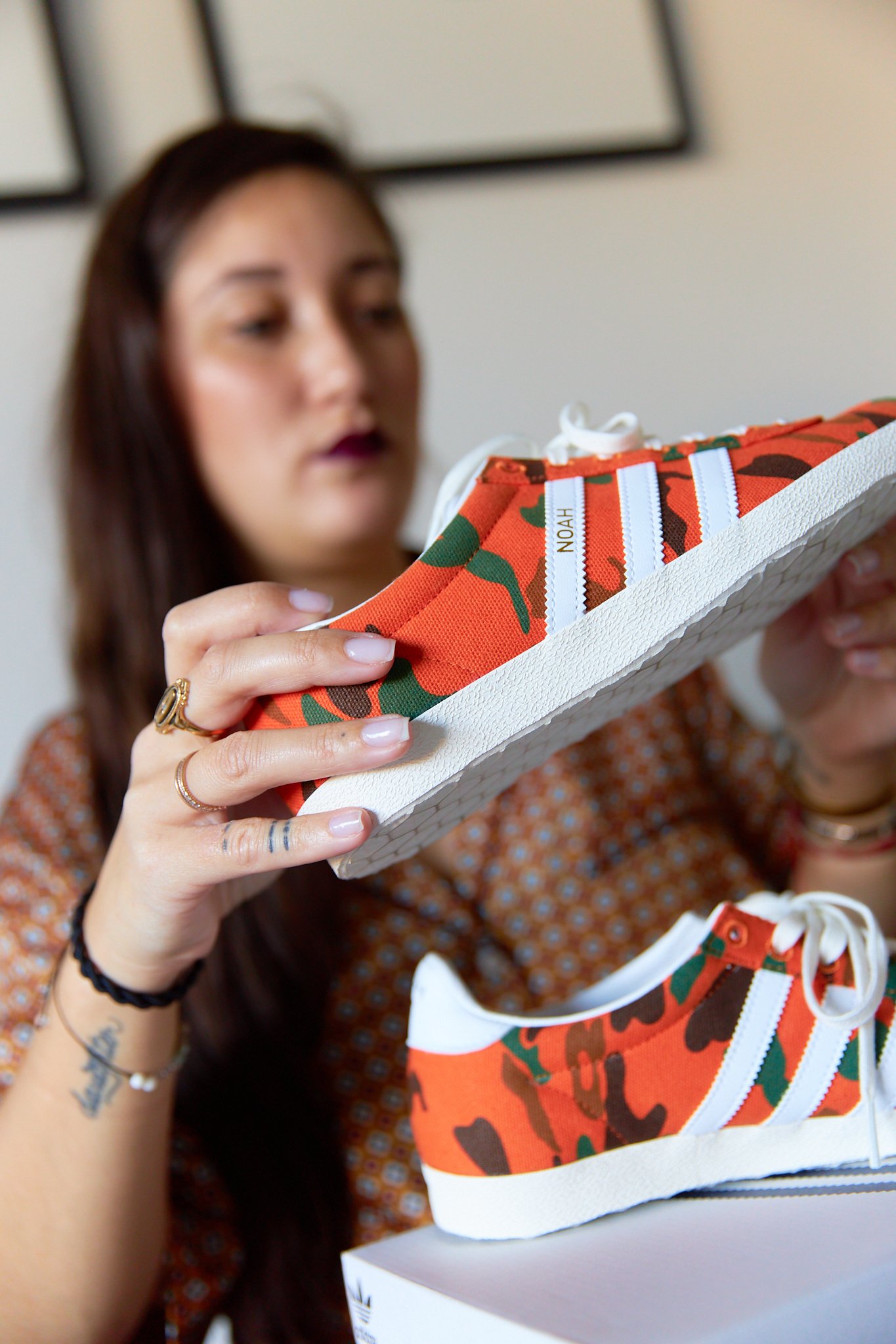 A woman examining a pair of Adidas sneakers with a camouflage pattern.