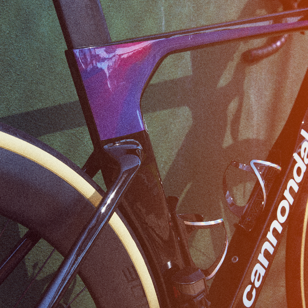 Close-up of a Cannondale road bicycle frame and front tire, with purple, black, and white colors, on a green surface.