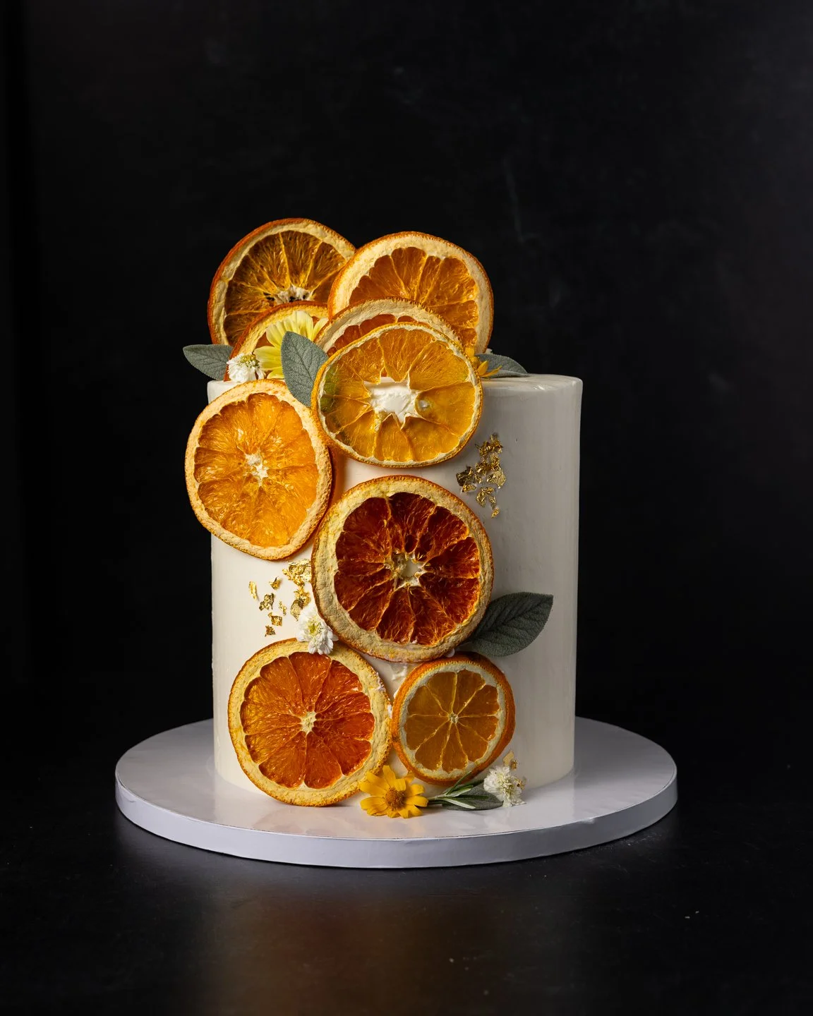 custom single tier wedding cutting cake decorated with dried orange slices, fresh edible greenery, and edible gold flakes