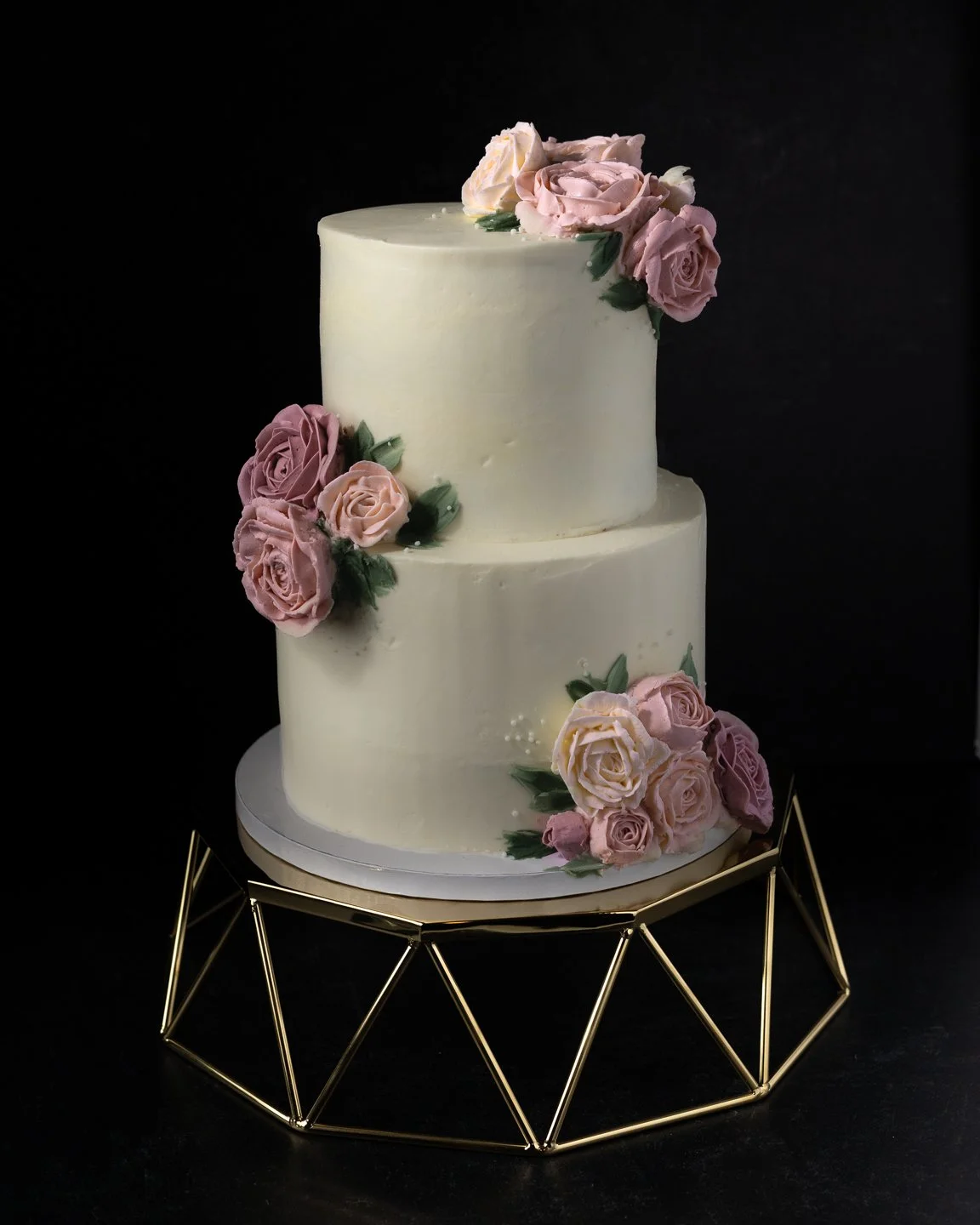 Custom two tiered luxury wedding cake decorated with hand piped buttercream florals in shades of blush on a specialty cake stand 