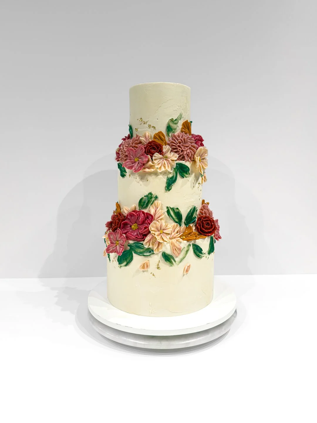 Custom three tiered wedding cake in Eugene OR decorated with buttercream flowers in shades of pink and orange
