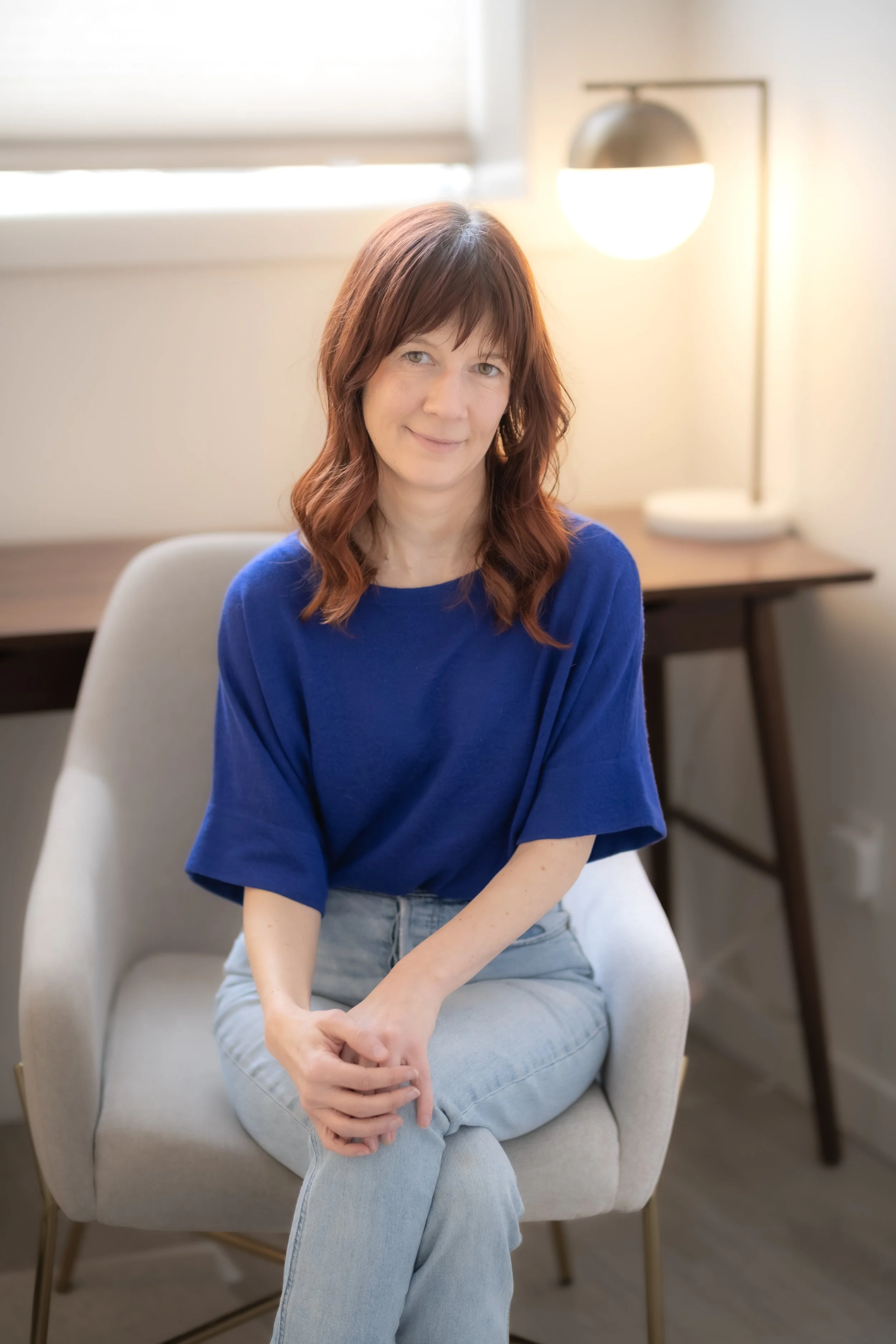 Smiling women sitting on a beige office chair near a desk with her legs crossed and hands on her knees