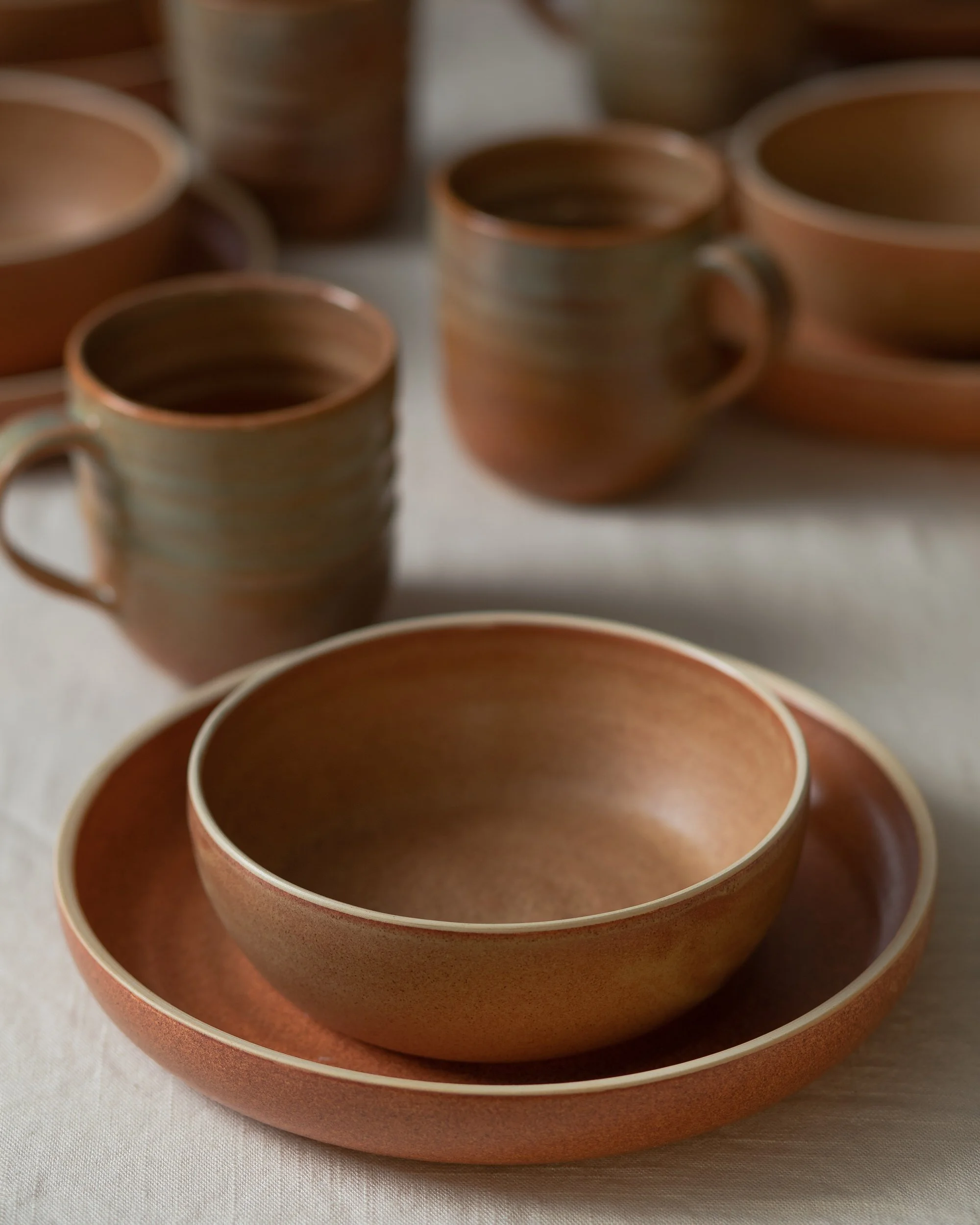 Tan ceramic mugs and bowls on a table together
