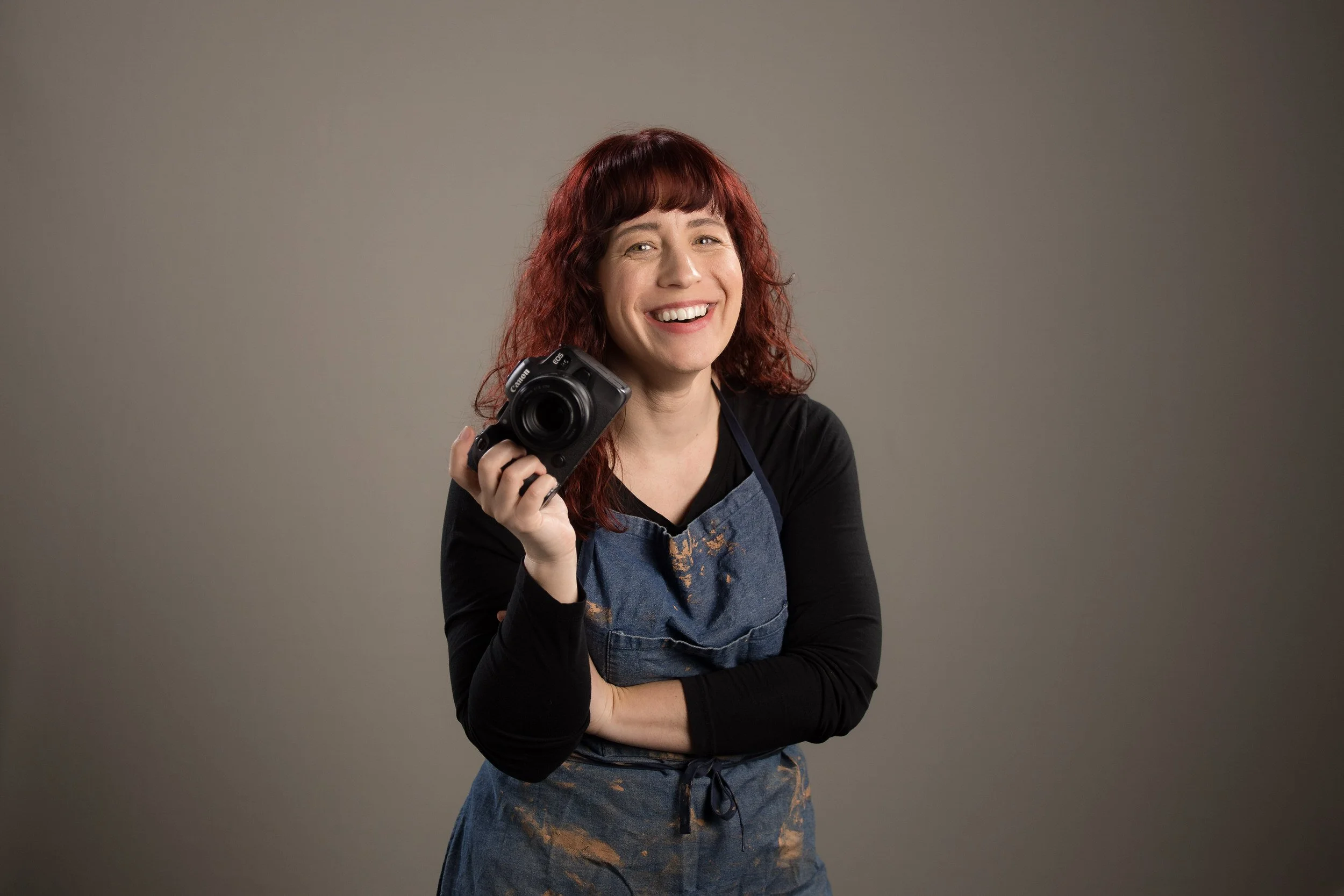 Rebecca smiling while holding a camera up with one hand