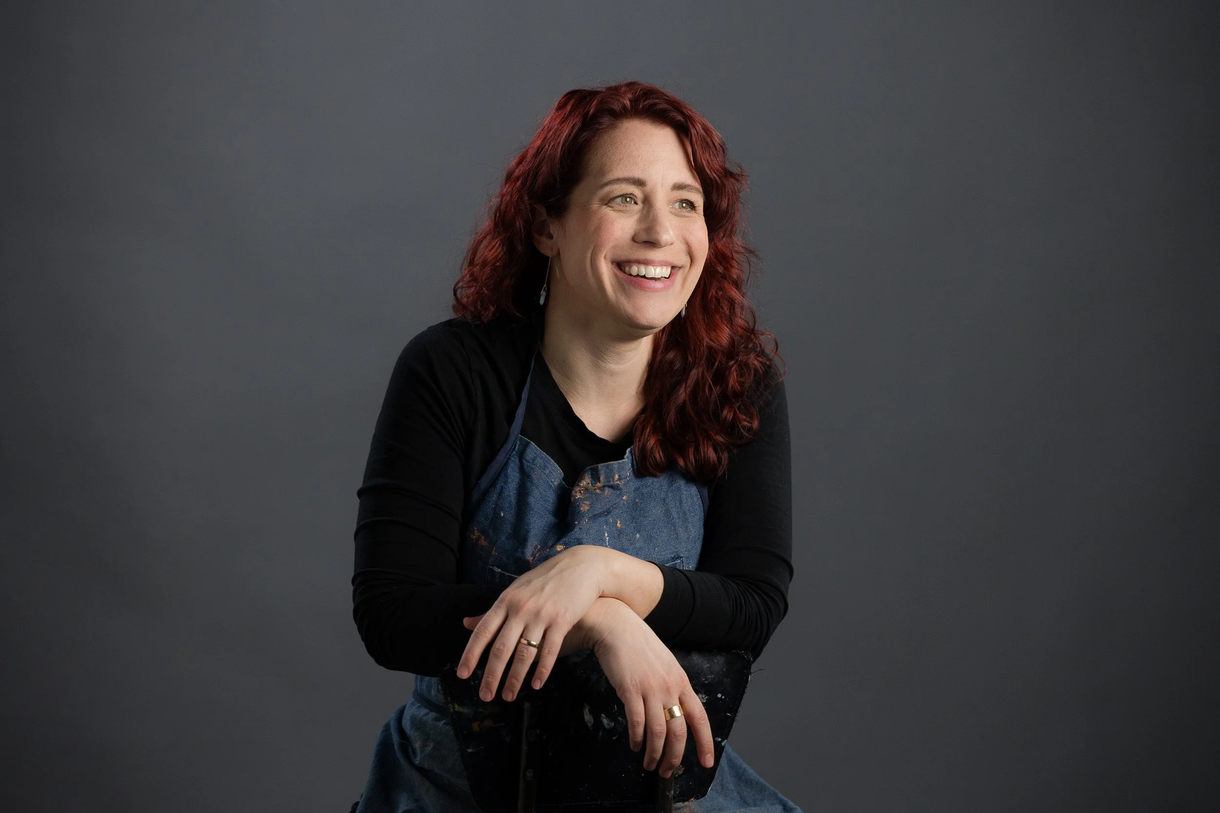 Rebecca smiling while she sits backwards in a chair