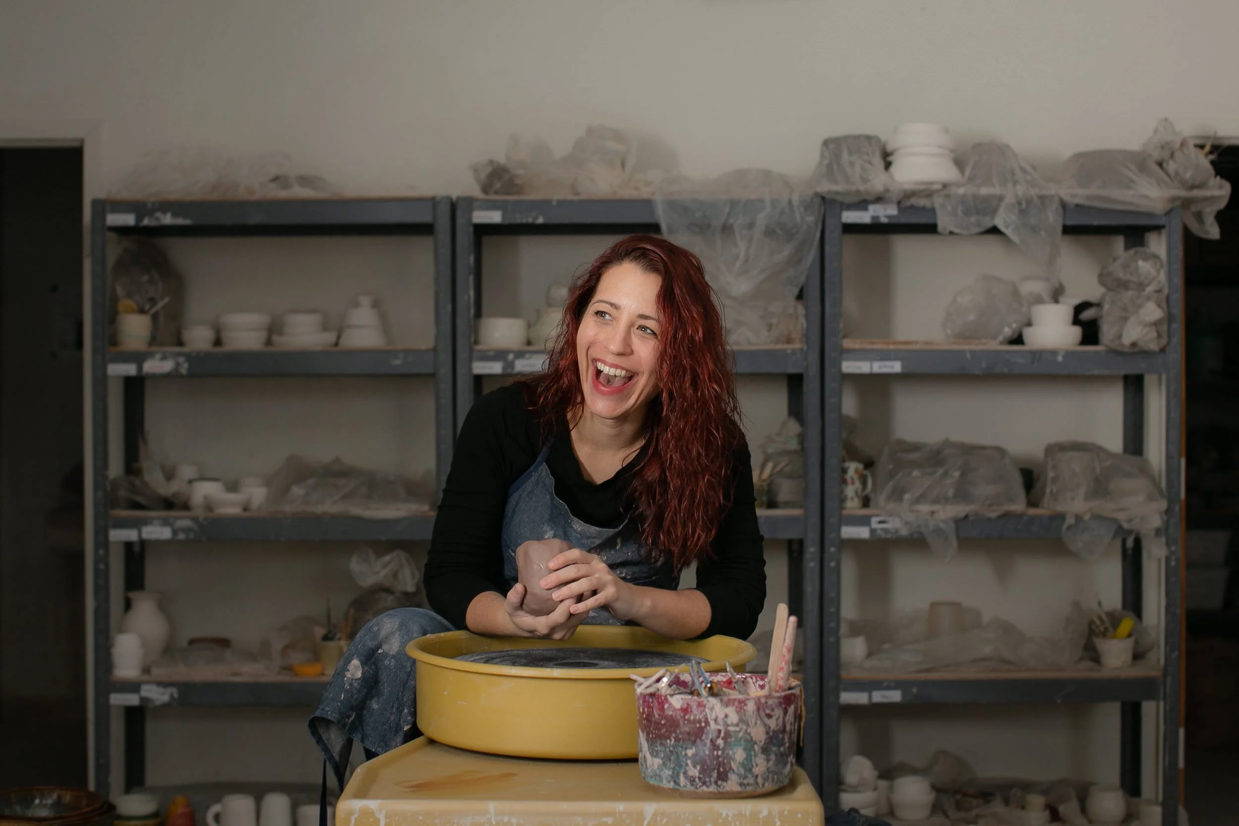 Rebecca smiling as she holds a ball of clay in a pottery studio