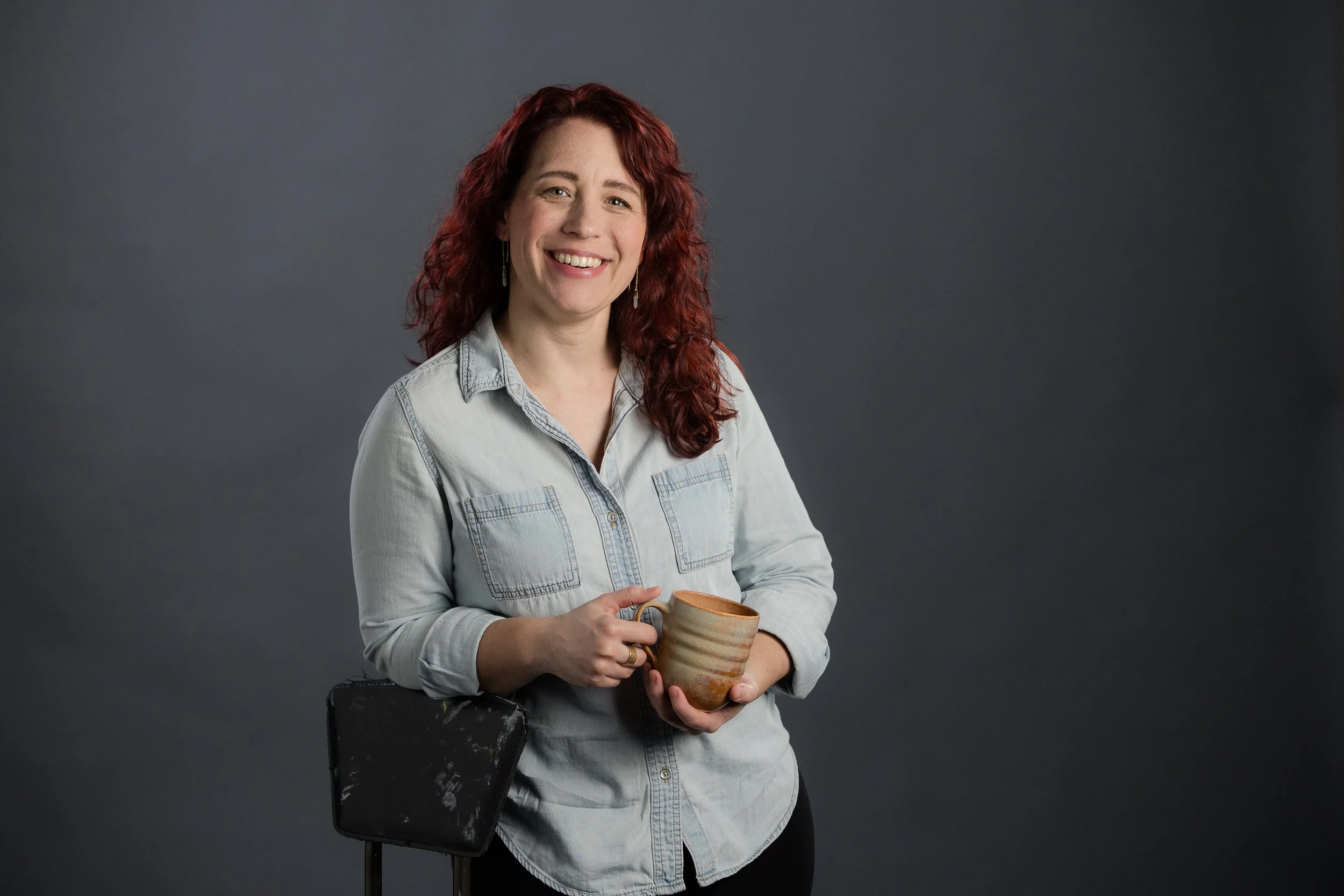 Rebecca holding a mug and smiling while leaning on a chair