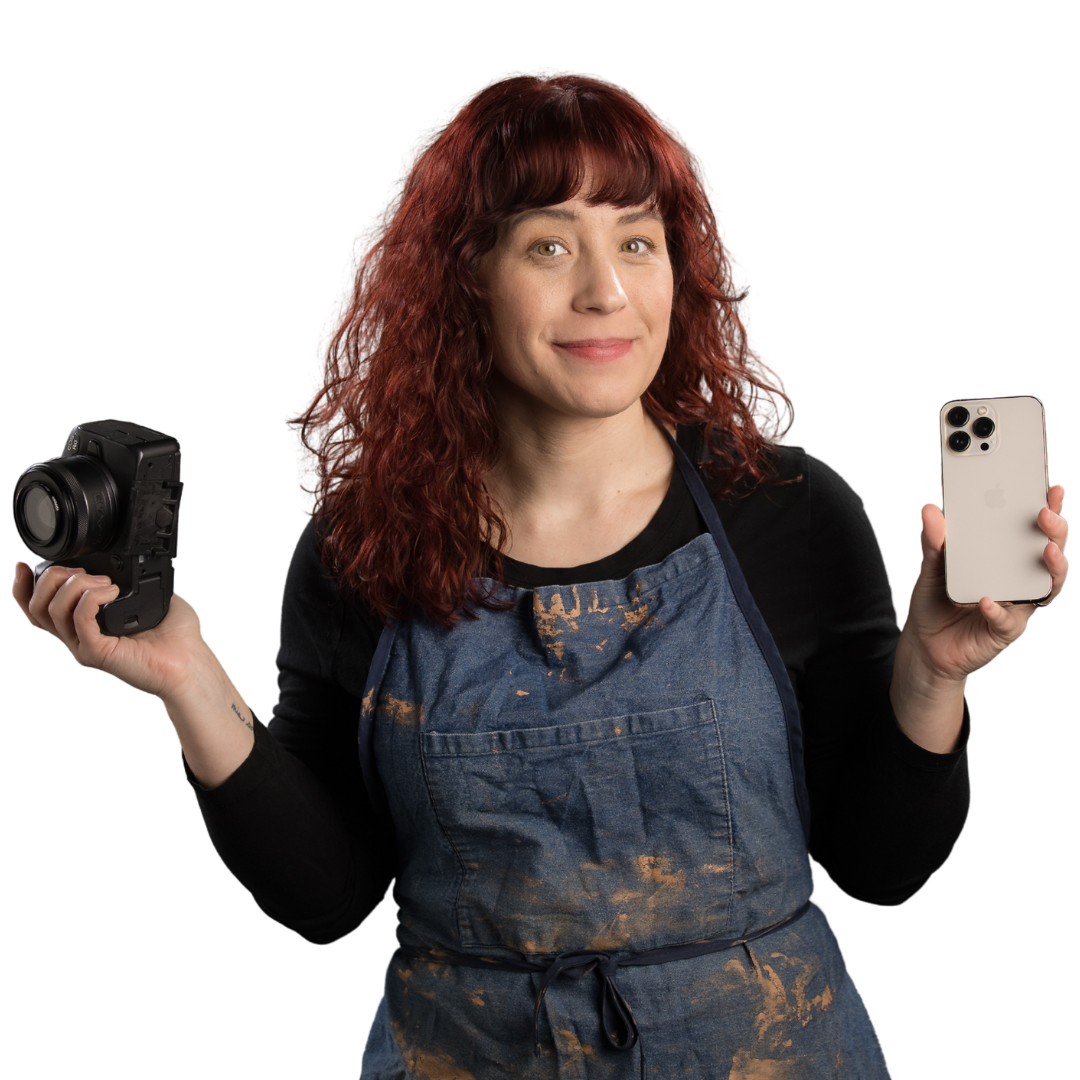 Rebecca smiling while holding a camera in one hand and a phone in the other