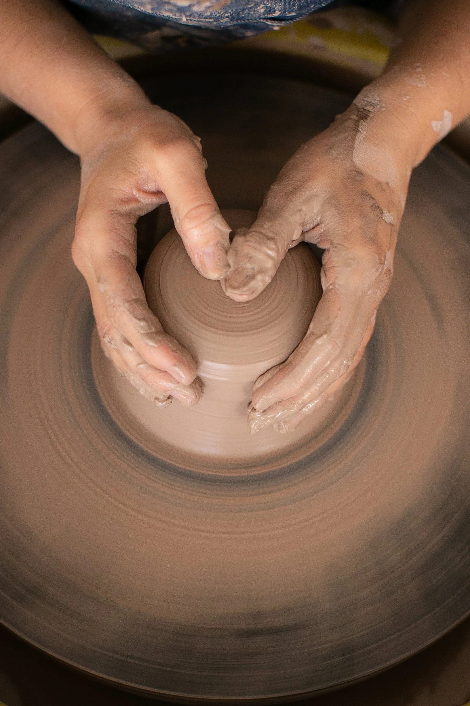 A person forming a ball of clay on a pottery wheel
