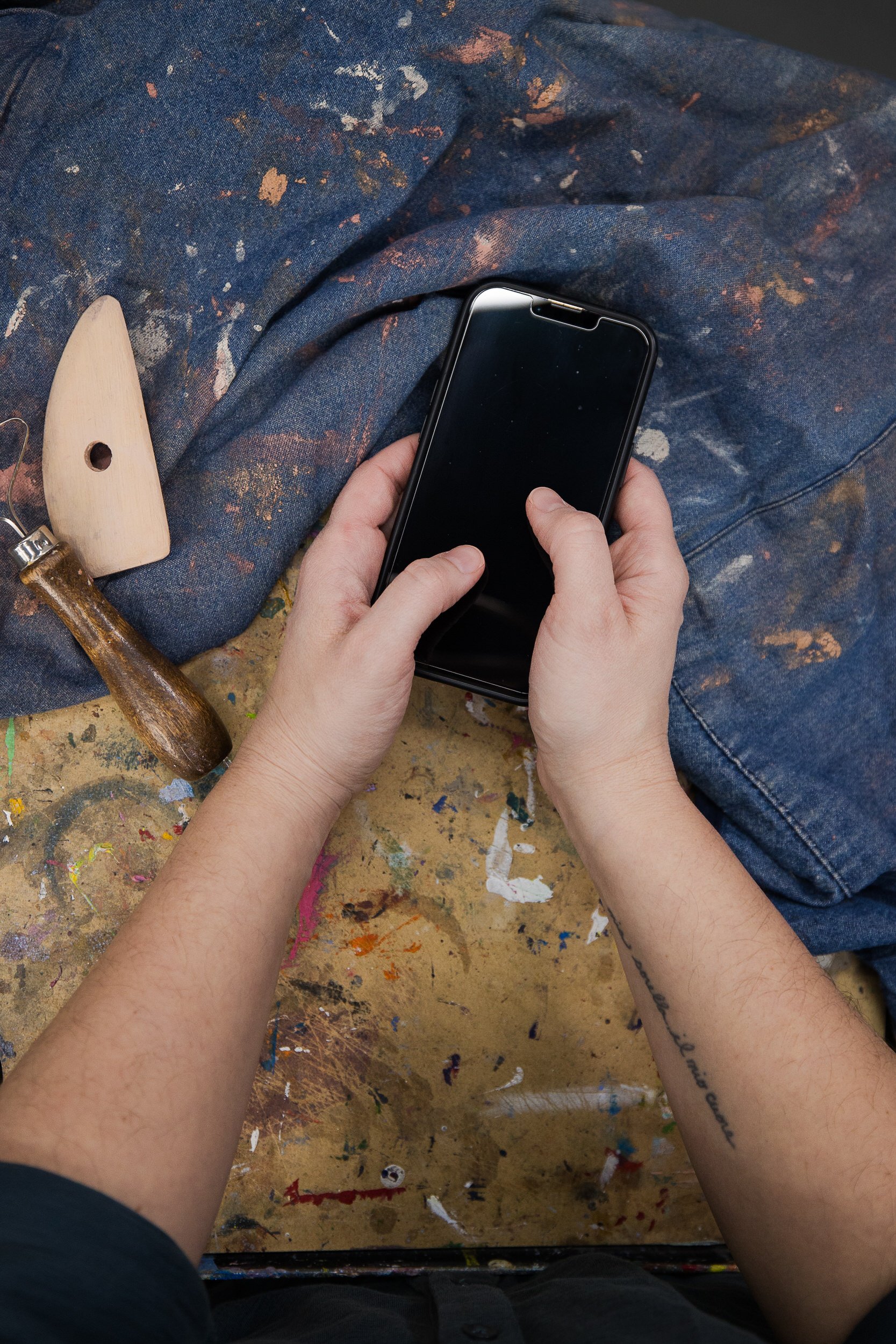 A person holding a phone while leaning on a paint covered table