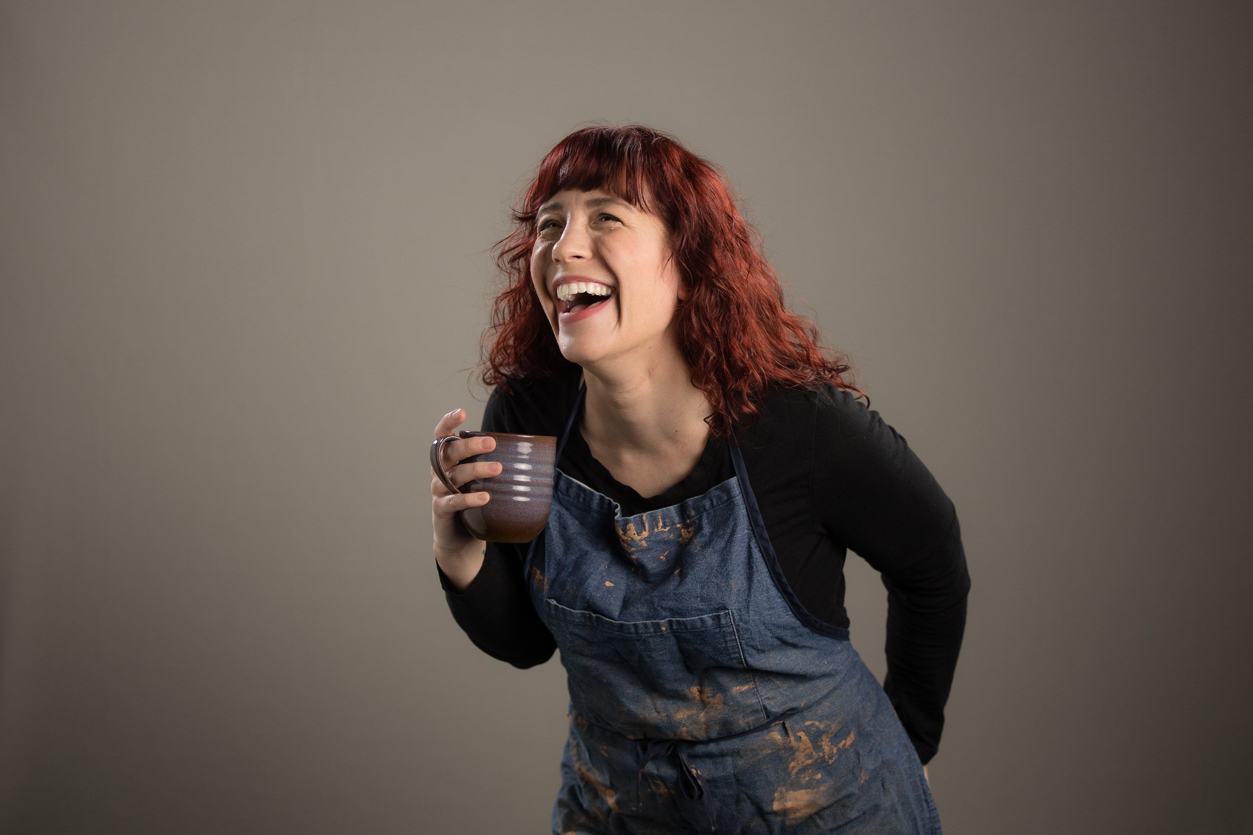 Rebecca laughing in an apron while holding a mug