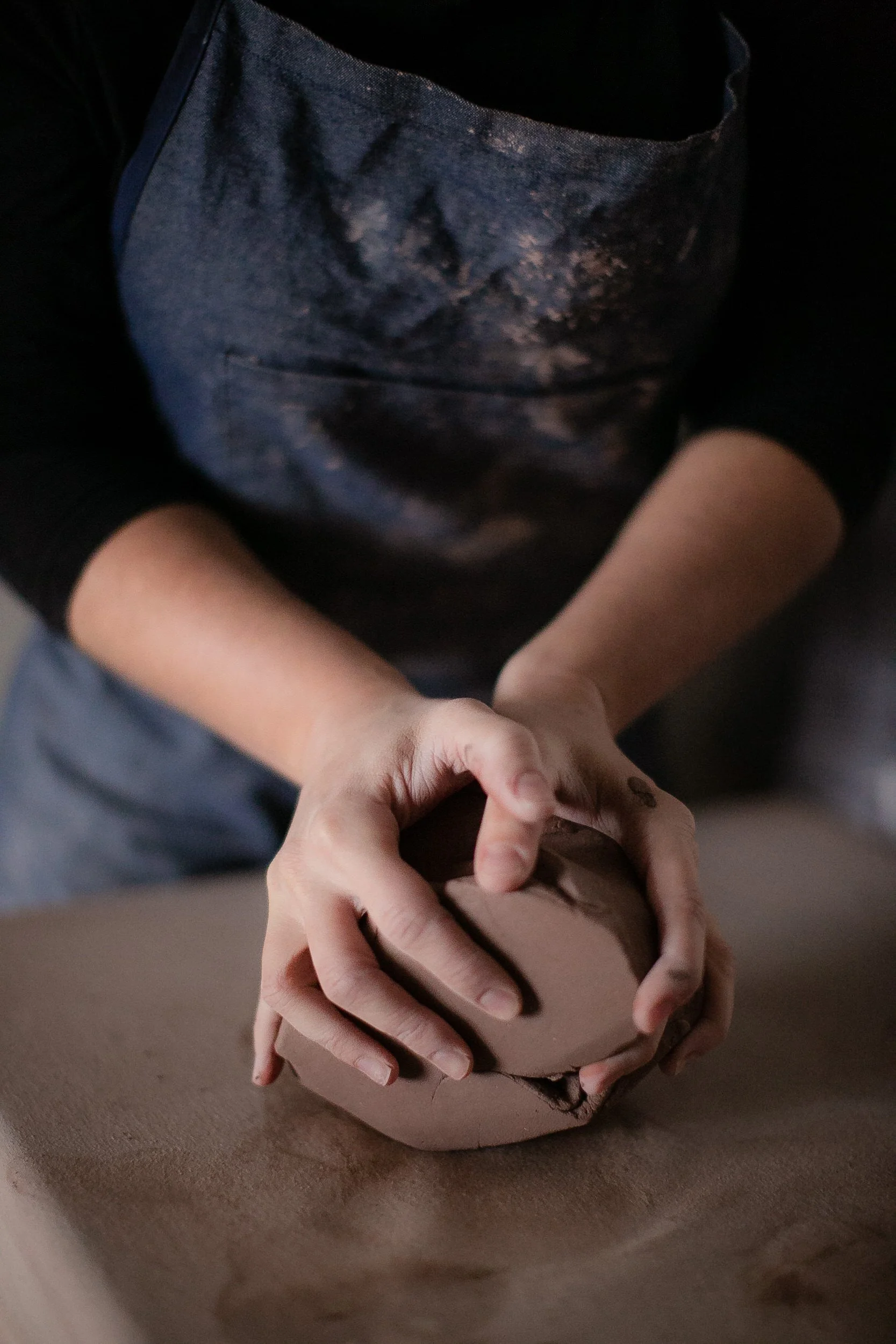 A person forming a ball of clay on a table