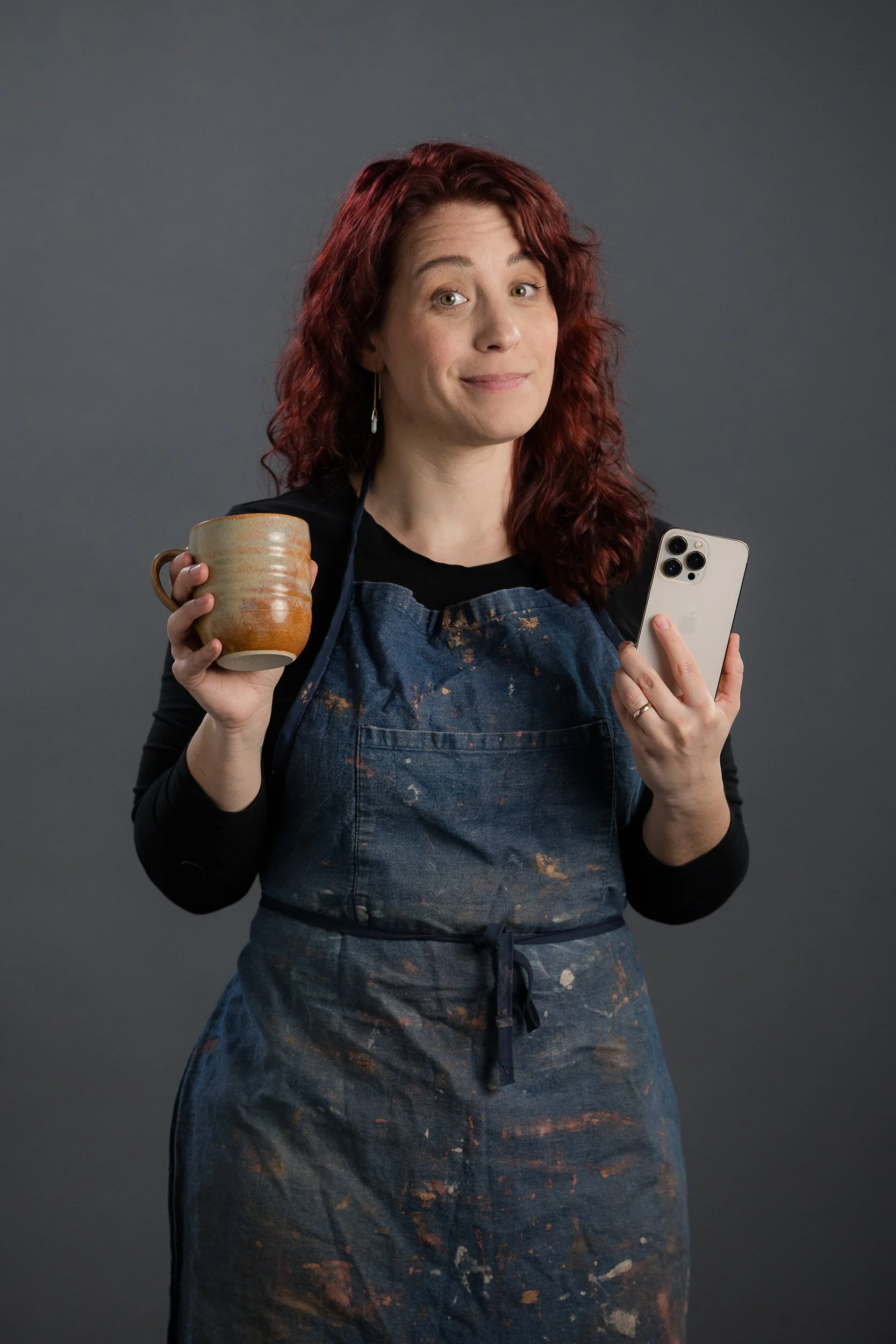 Rebecca smirking while holding a mug in one hand and a phone in the other