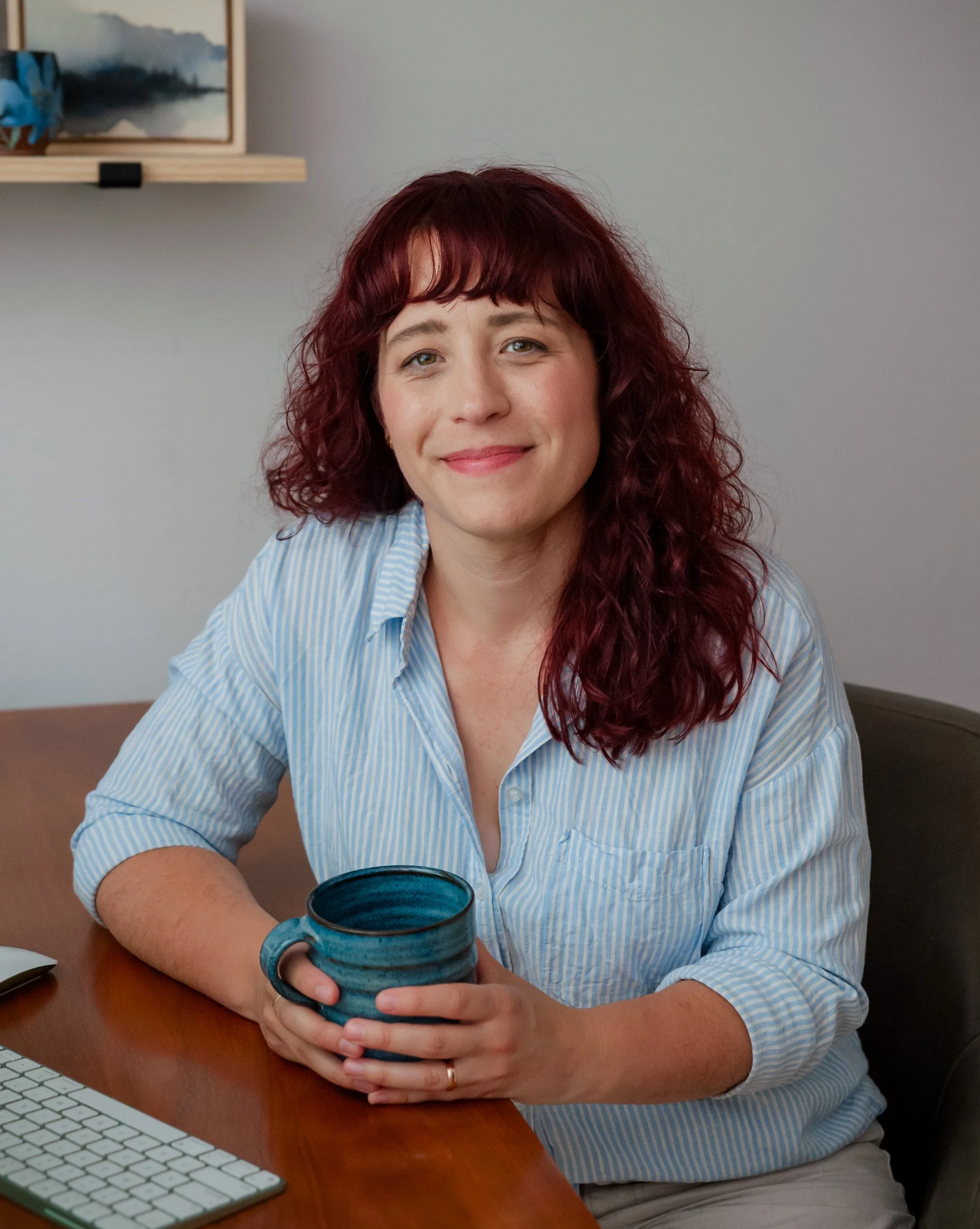 Rebecca sitting at a table holding a mug and smiling