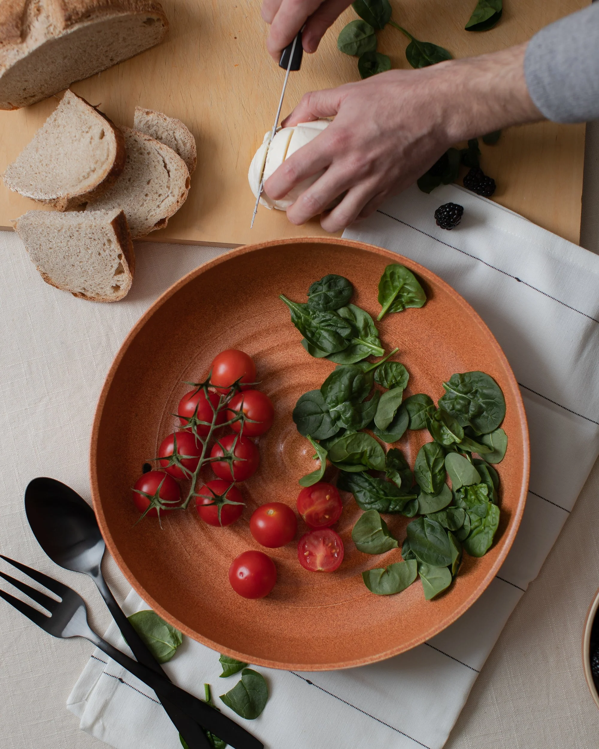 A person cutting mozzarella in front of a bowl with tomatoes and basil in it