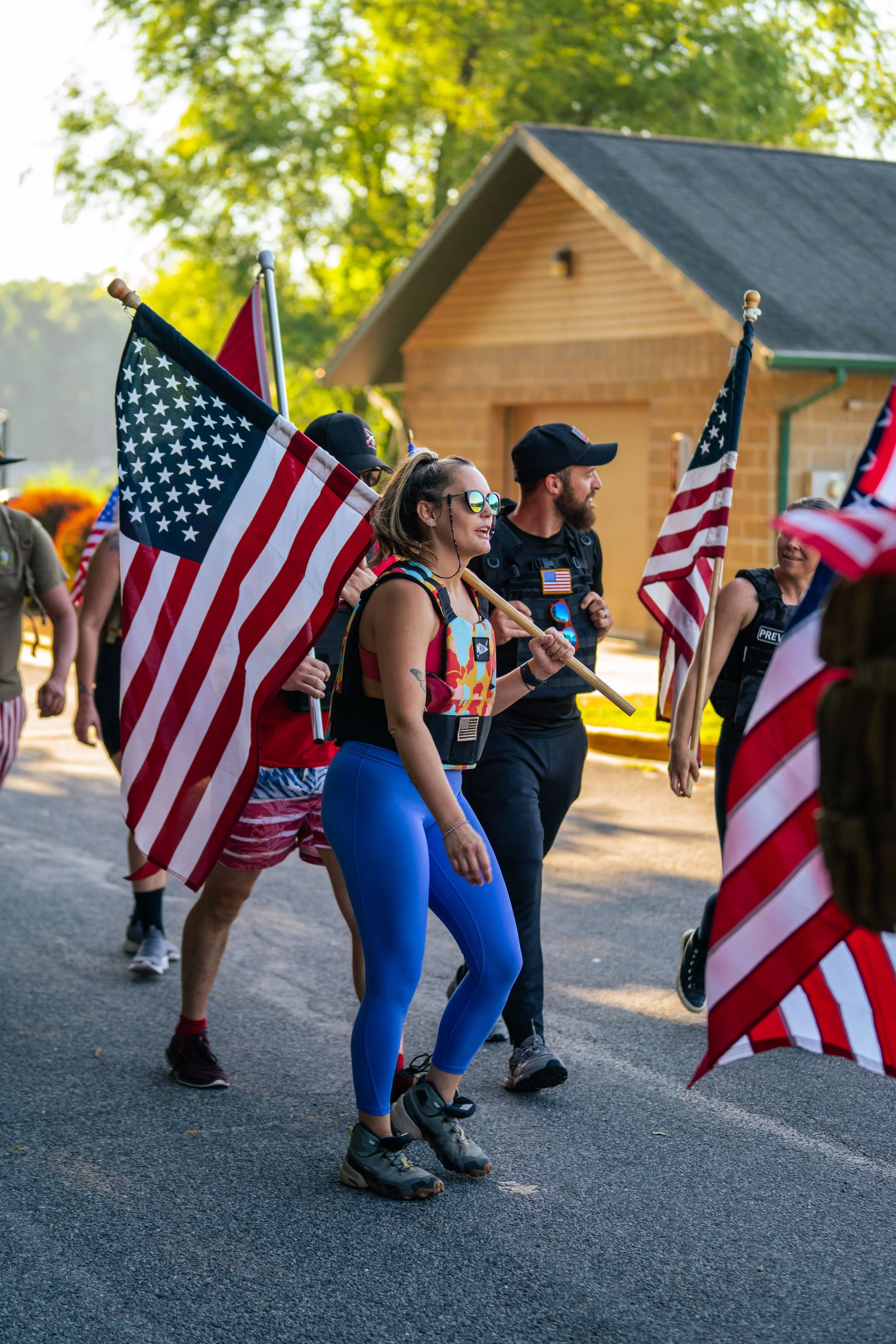 Group of people walking outdoors holding American flags, wearing patriotic clothing.