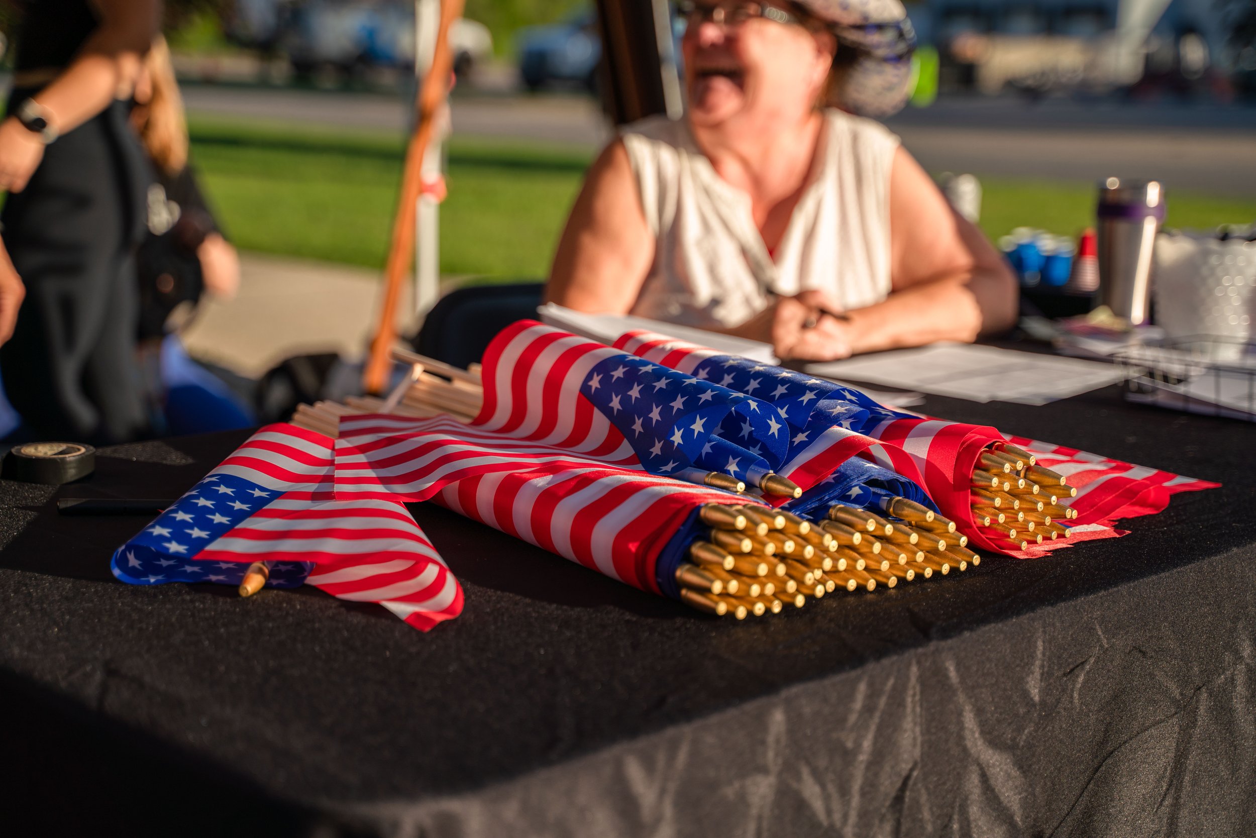 Table with American flags on small poles, outdoor setting, person with hat in background.